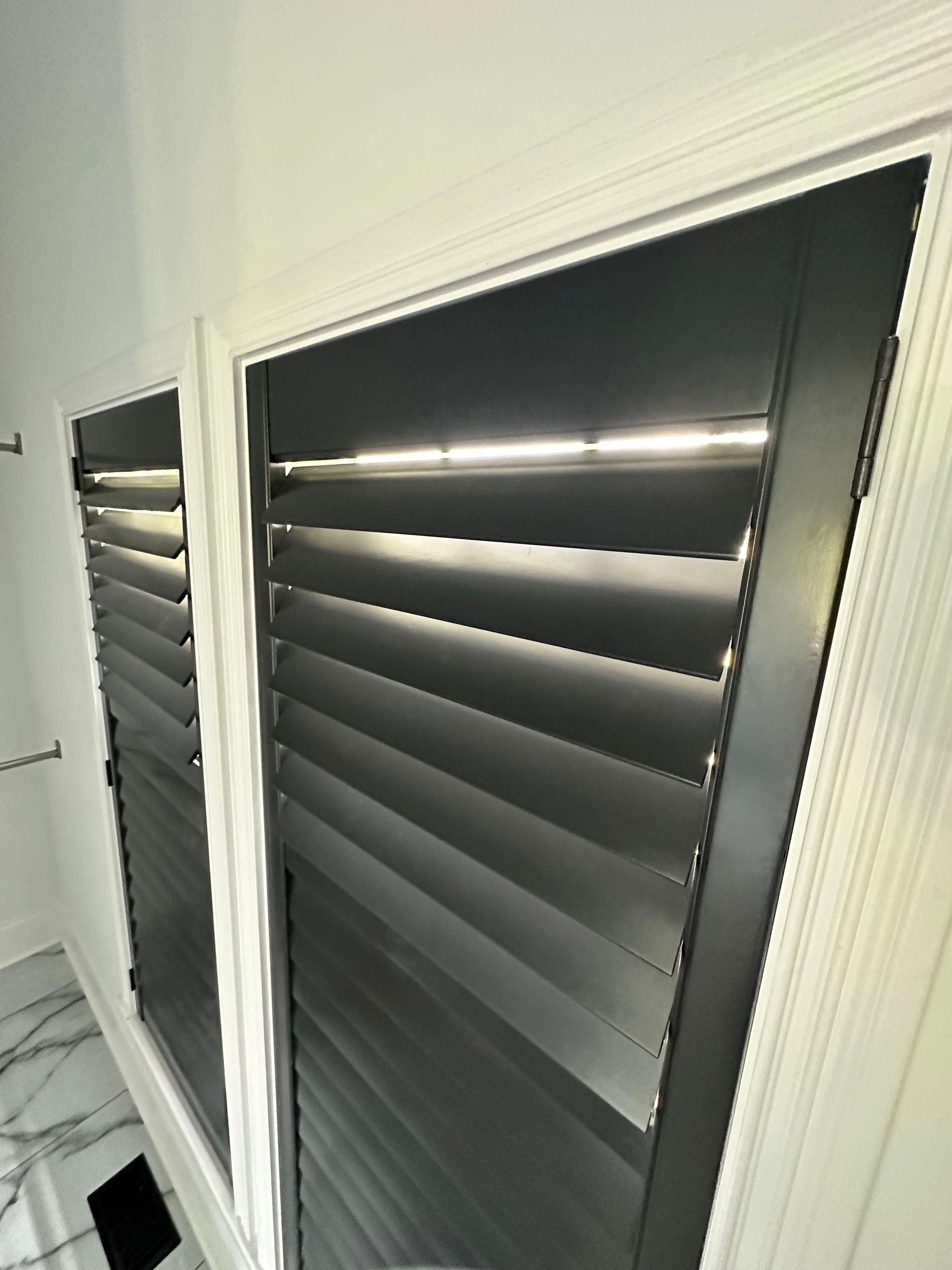 Black louvered shutters inside white-framed windows in a bright bathroom.