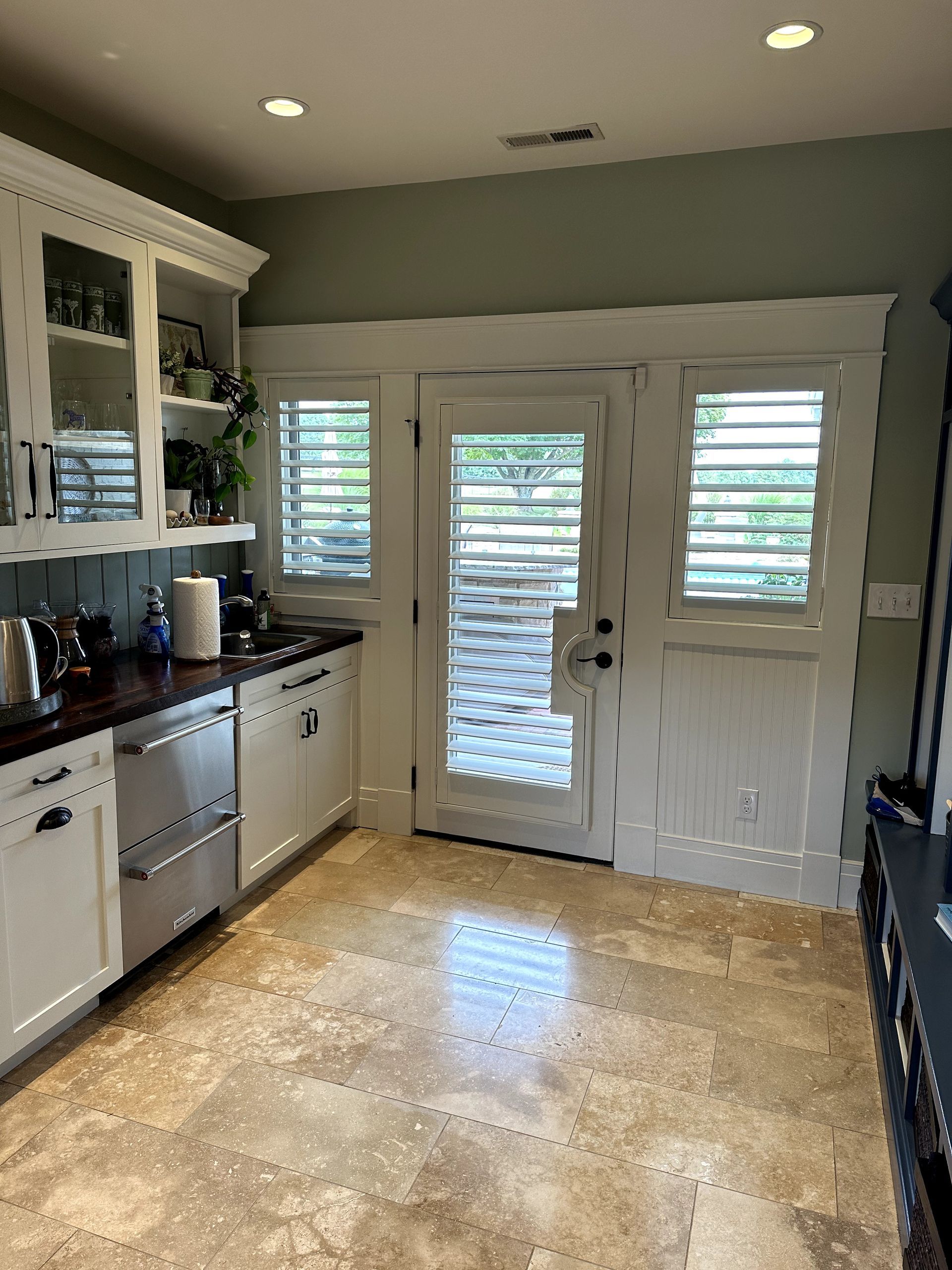 A bright kitchen with white cabinets, a dishwasher, and doors with shutter-style blinds.