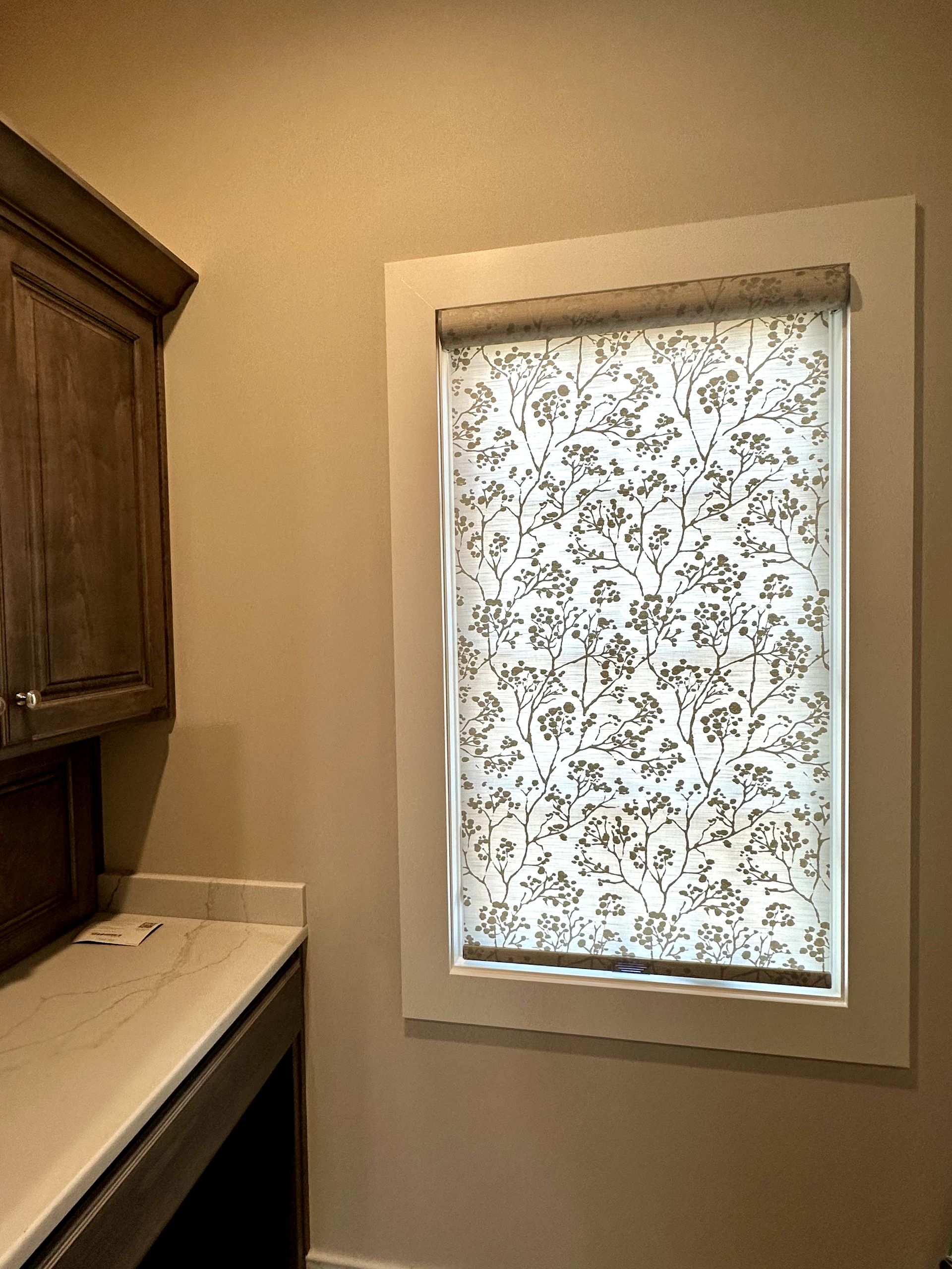 Window with a floral patterned shade in a room with a cabinet and countertop.