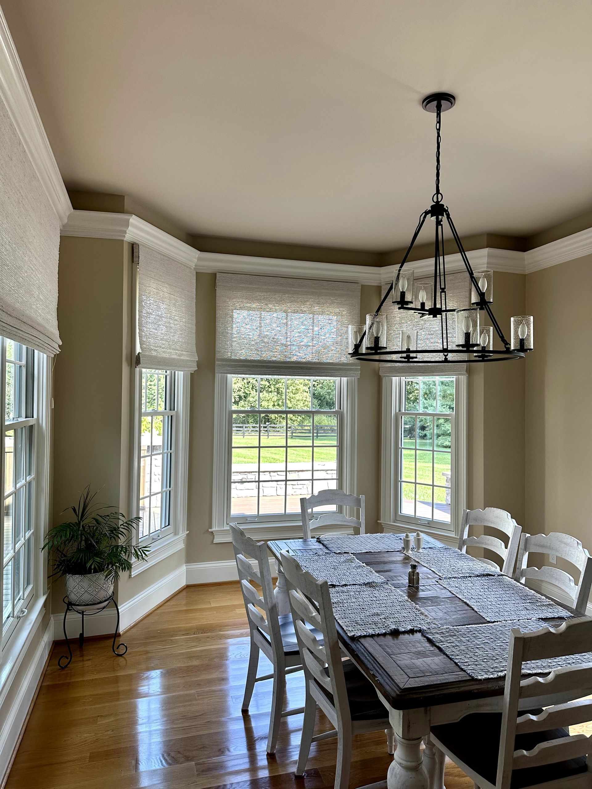 Dining room with a table, white chairs, chandelier, and Roman shades.