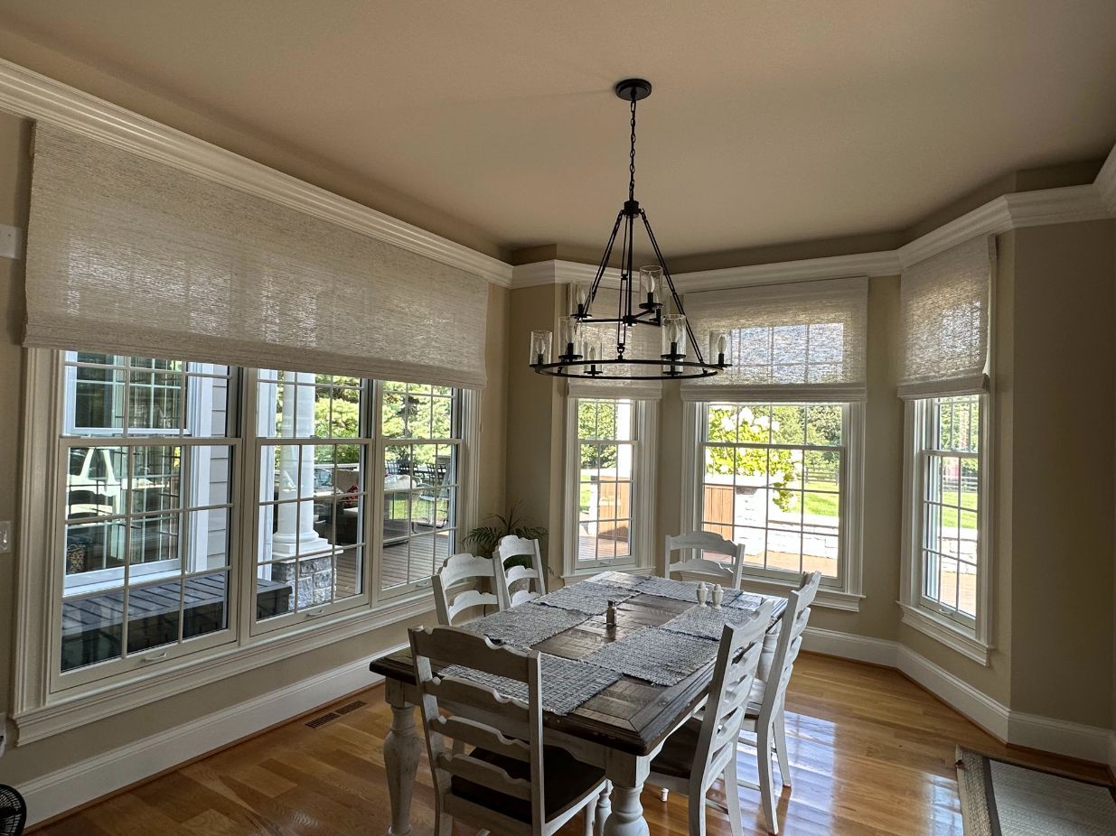 Dining room with a chandelier, table, and chairs. Windows with light shades.