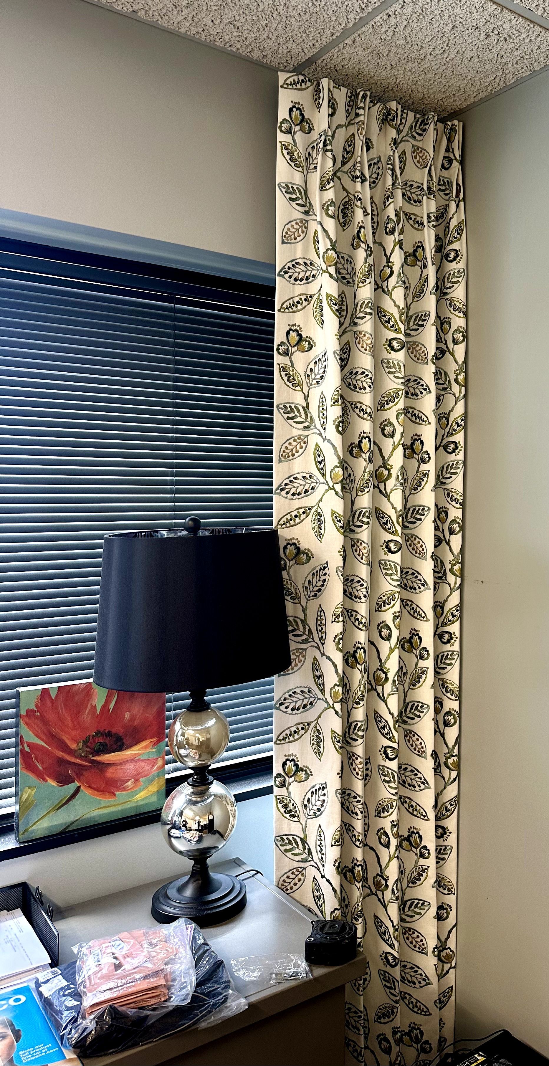 Black and white floral curtain next to a window with a lamp and artwork on the sill.