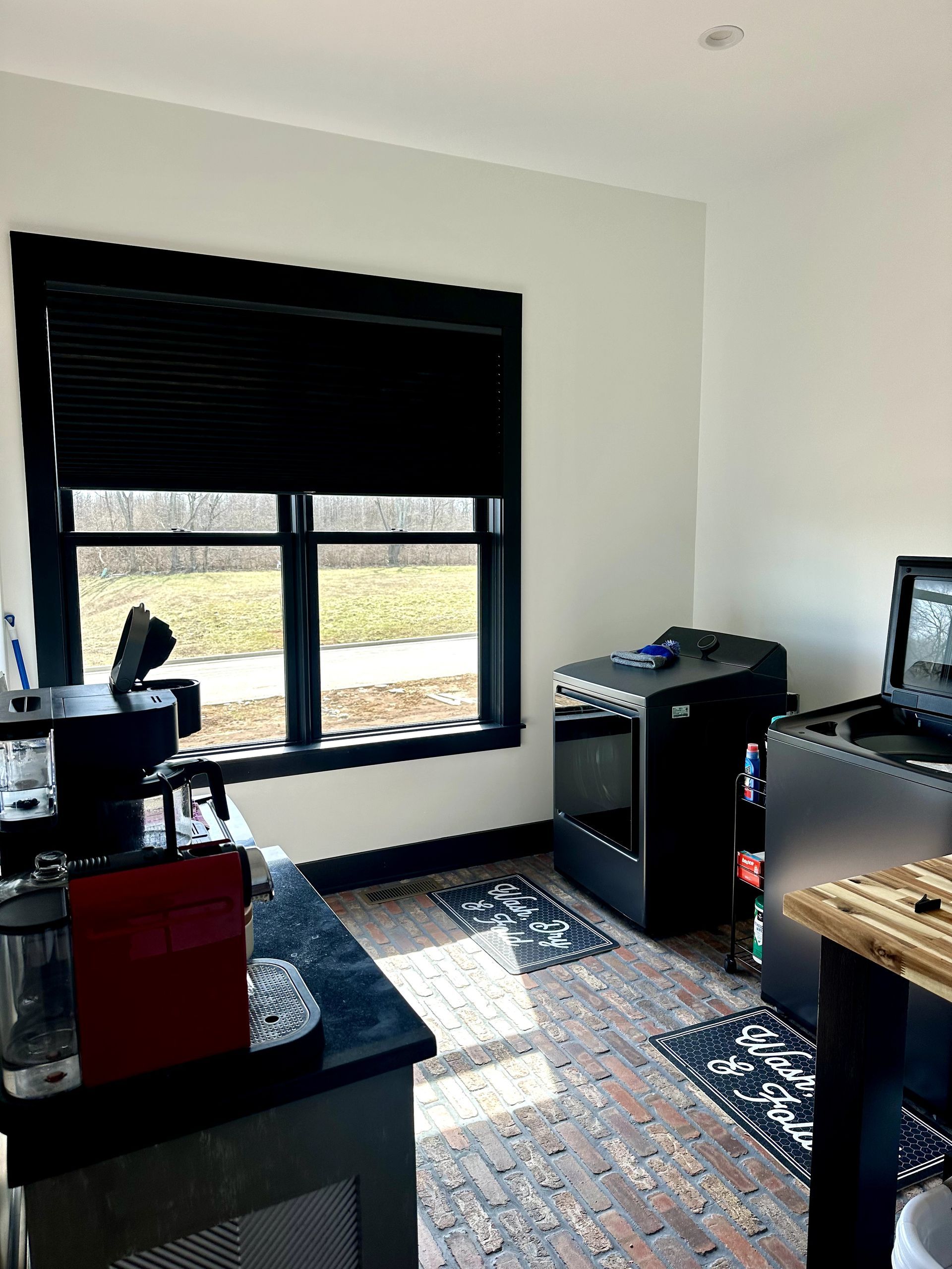 Room with a black-framed window and blinds. A black counter and equipment are nearby.