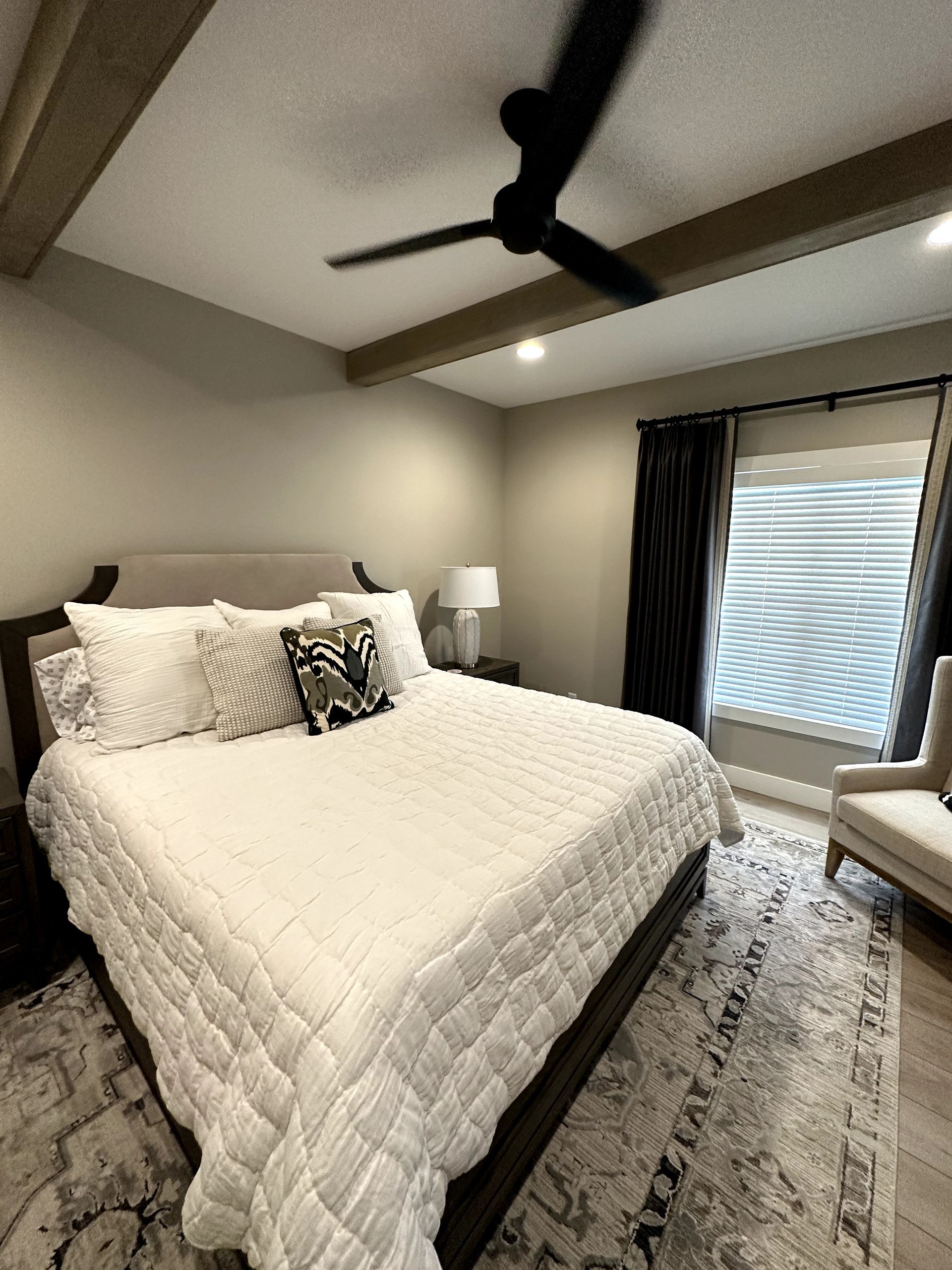 Bedroom with a large bed, rug, window, dark curtains, and a ceiling fan.