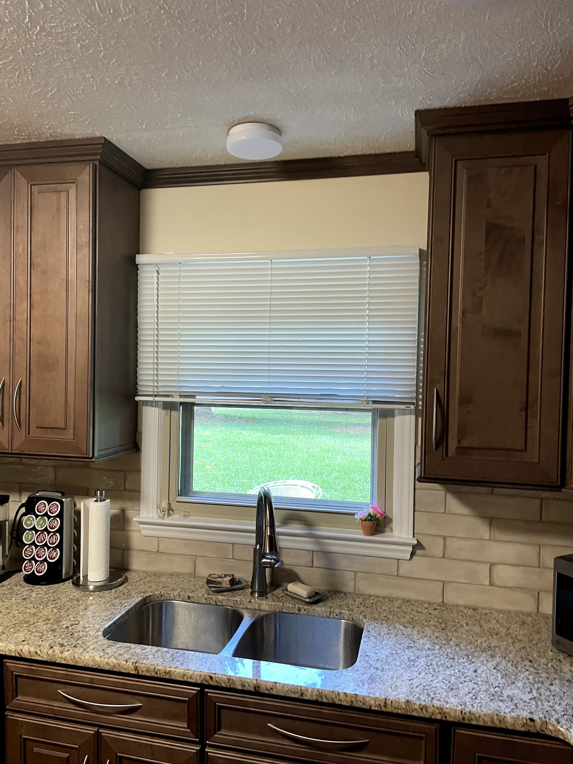 Kitchen sink with blinds and cabinets. Green grass visible outside the window.