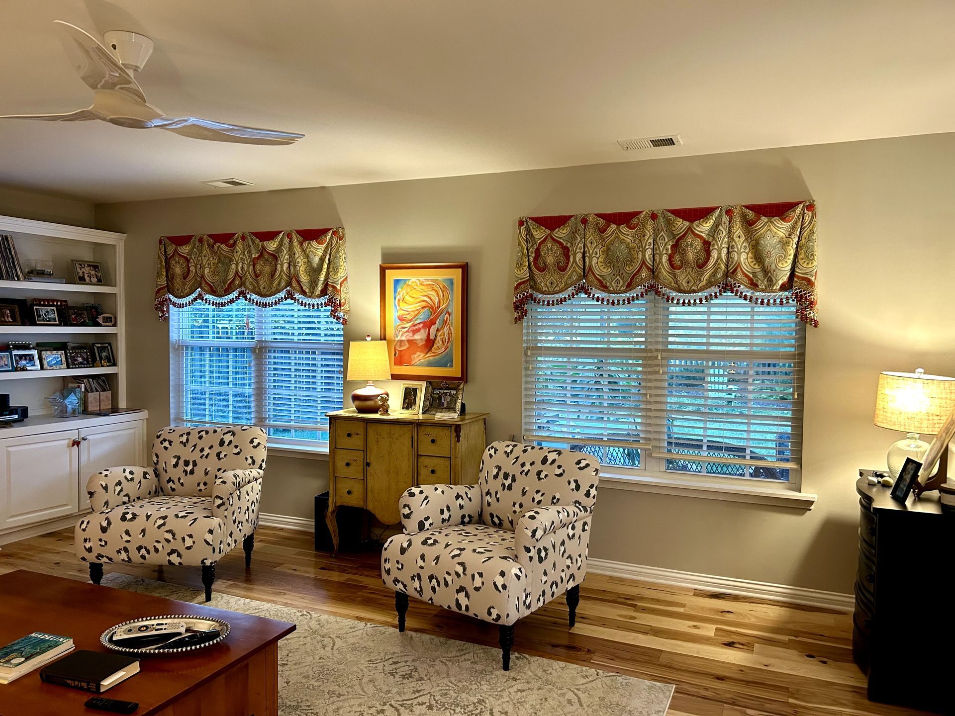 Living room with patterned armchairs, windows with ornate valances, and a wood floor.