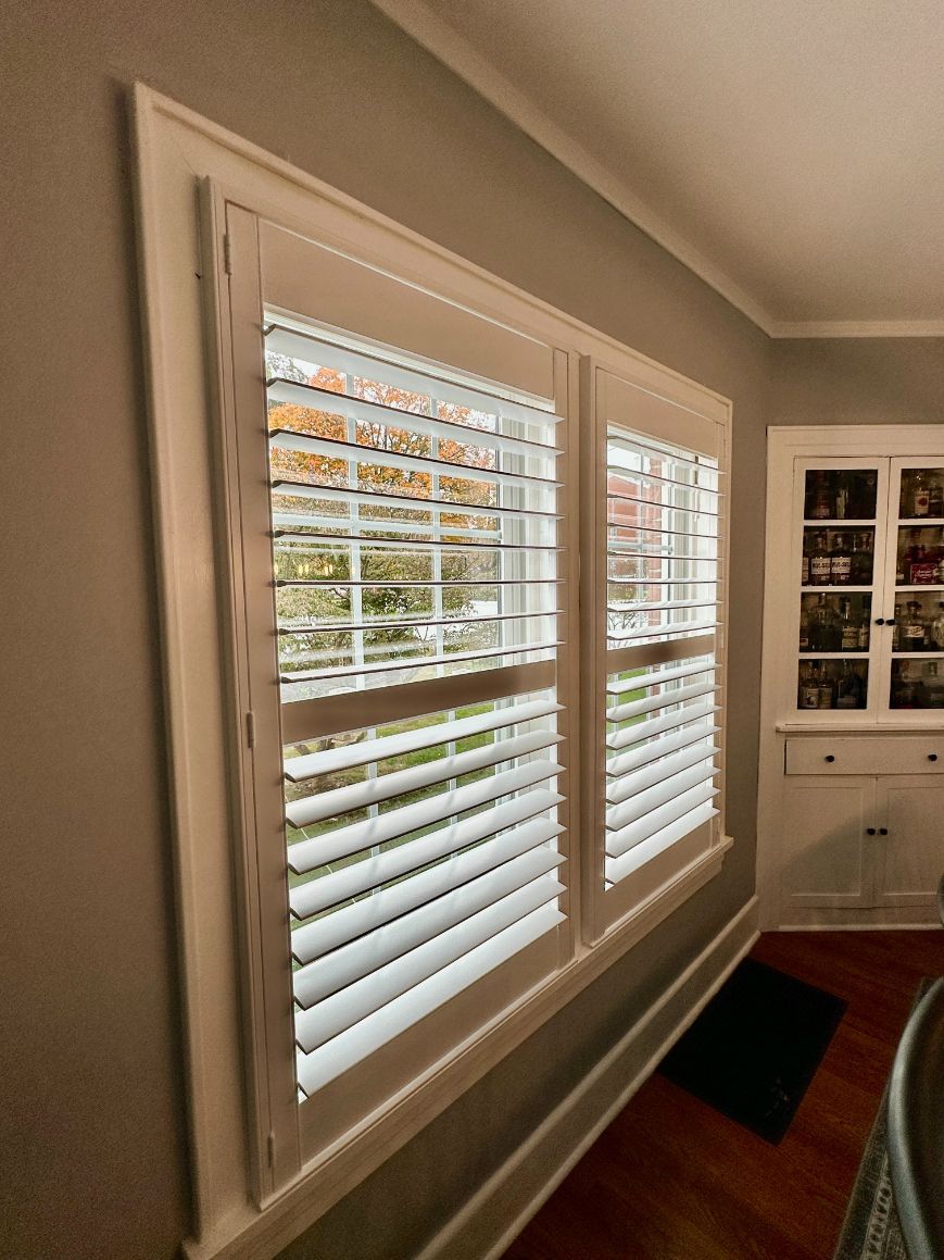 White plantation shutters installed on a double window in a room with gray walls and a wooden floor.