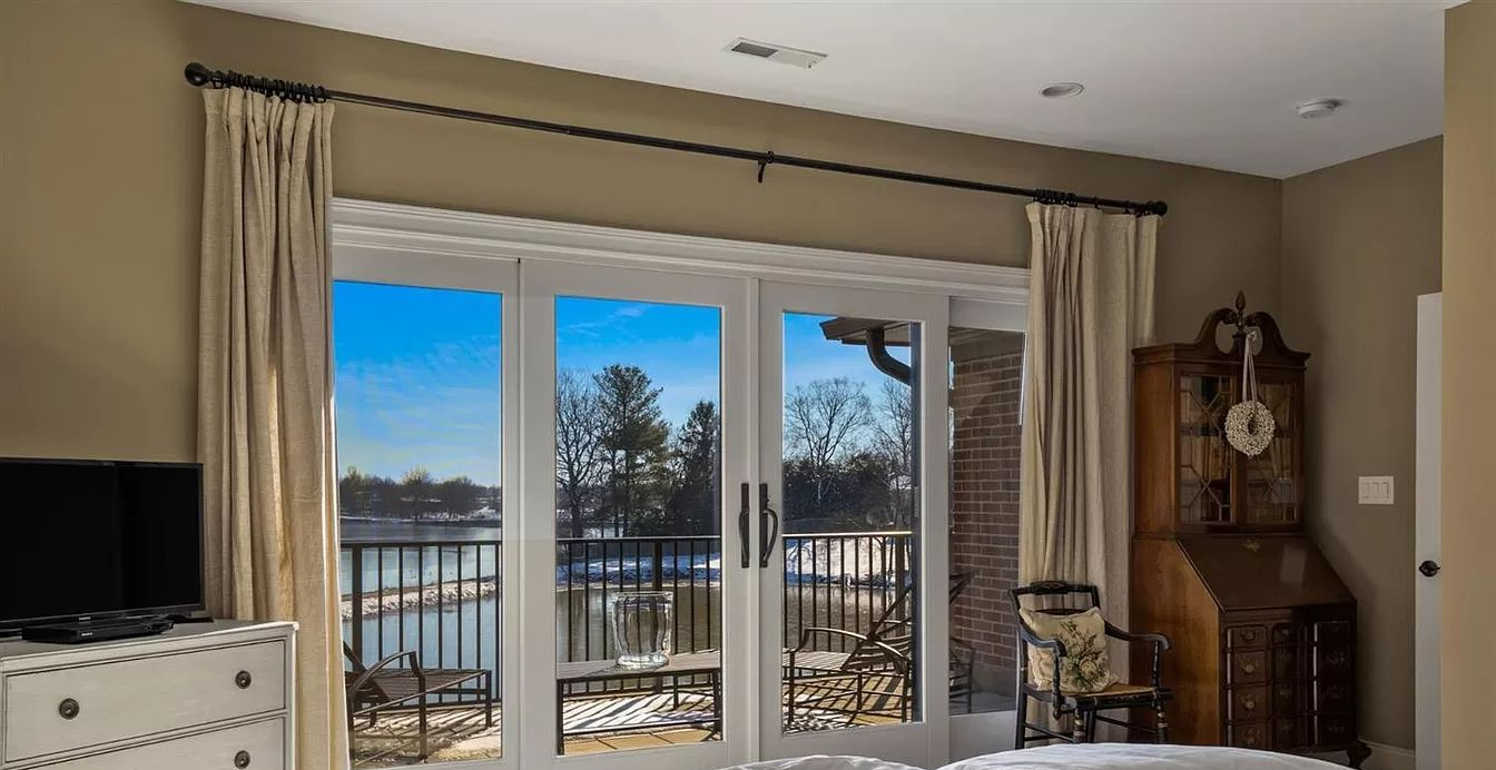 Living room with lake view through sliding glass doors, beige drapery, and a wooden clock cabinet