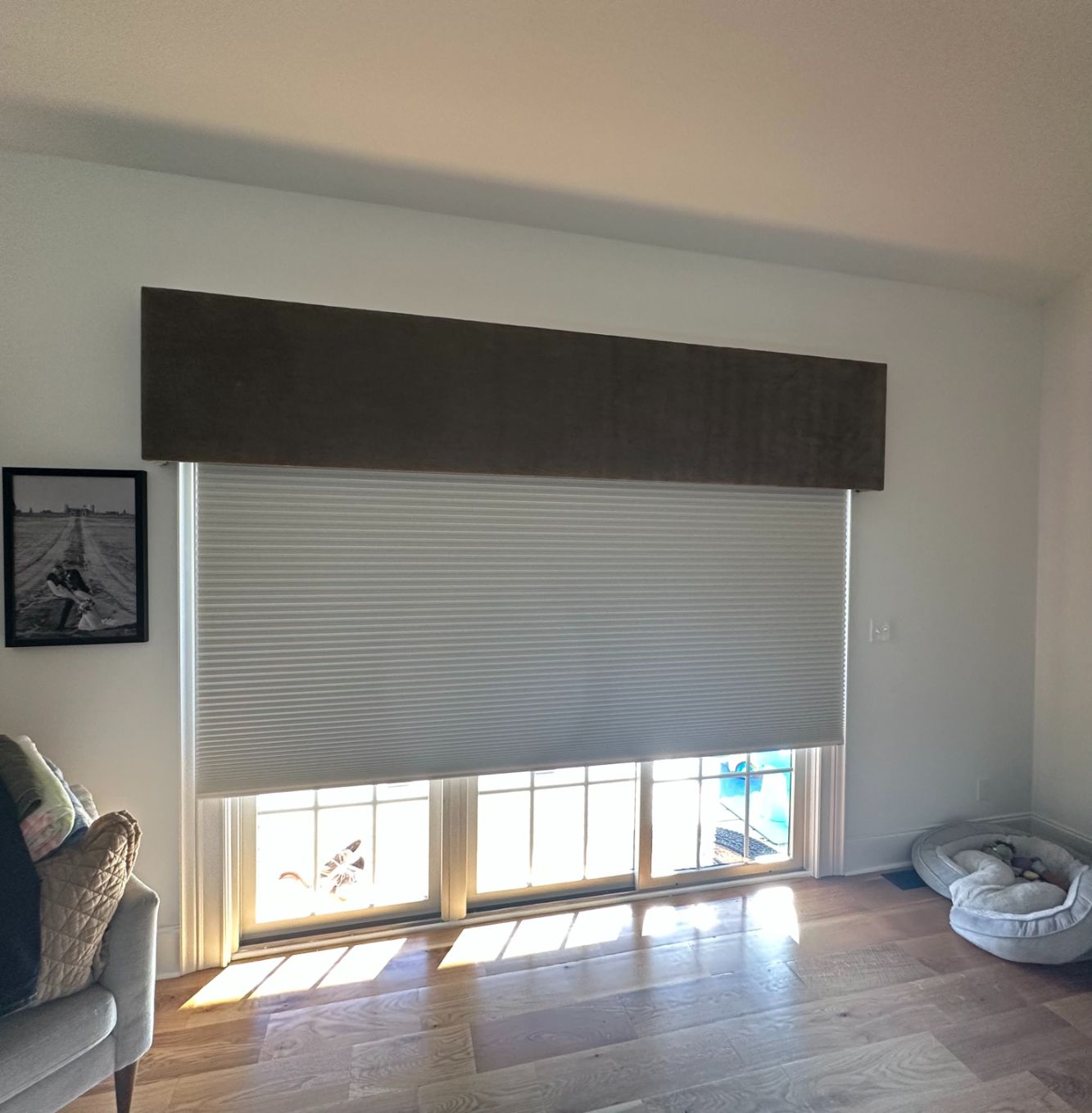 Window with closed light gray pleated blinds, brown valance, and sunshine.