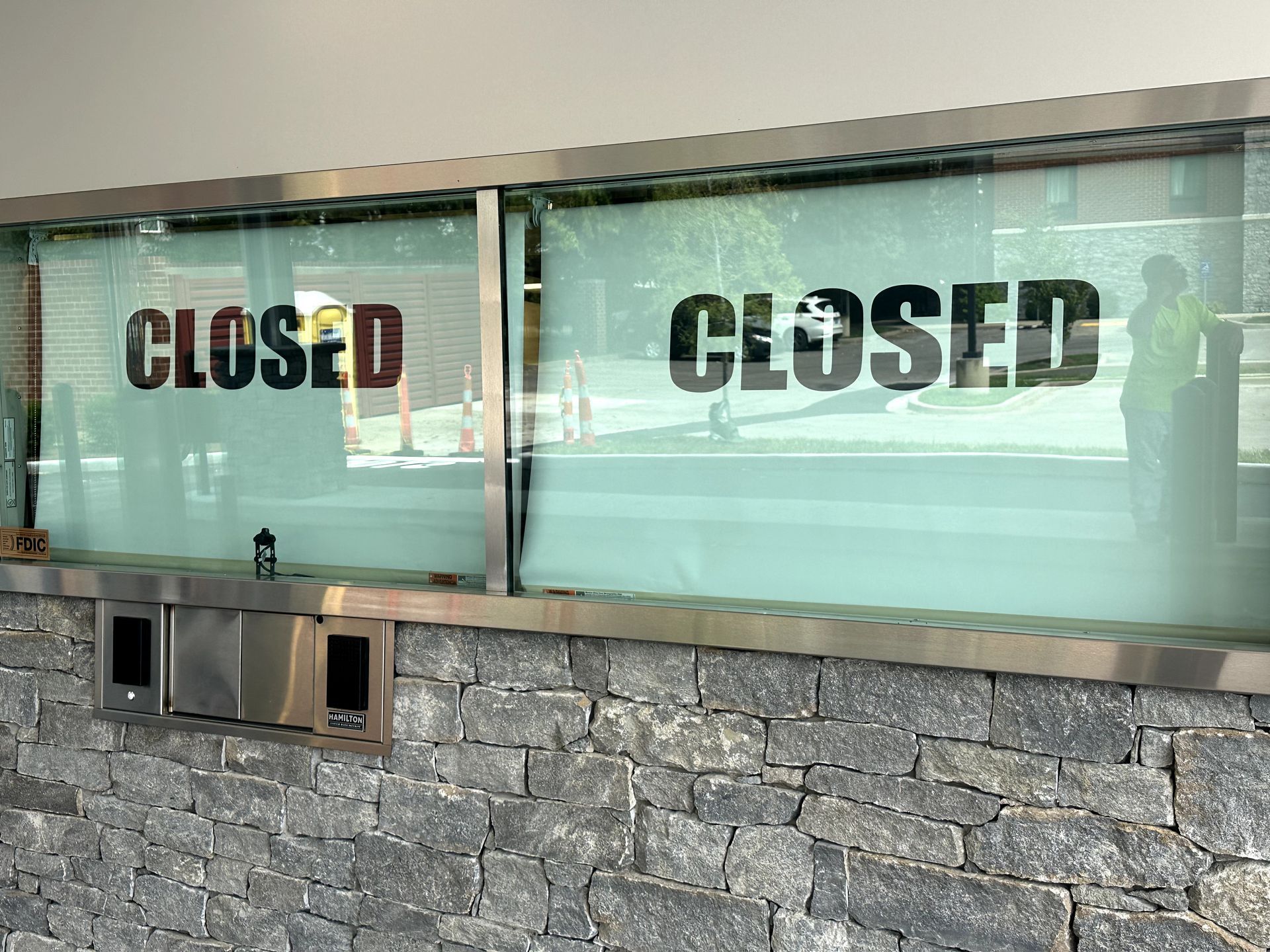 Closed sign on a glass window of a building with a stone wall below.