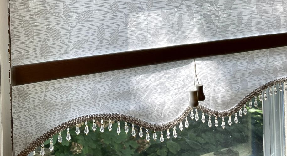 Window shade with beaded trim, brown wooden rod, and pull cords.
