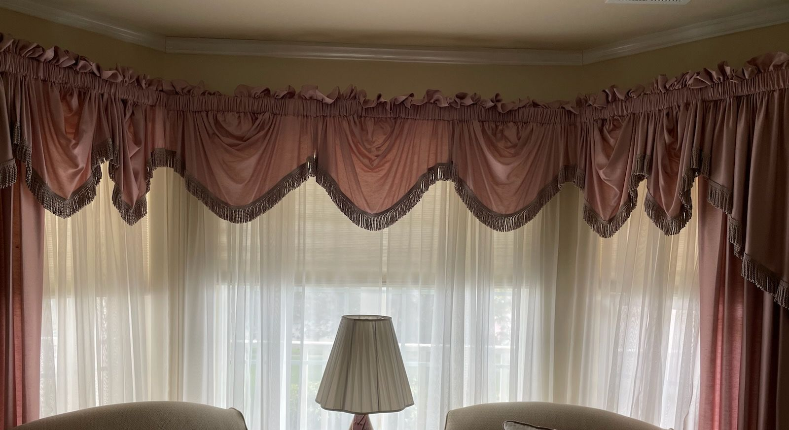 Pink and cream draped window curtains with a valance. A lamp sits below the window.