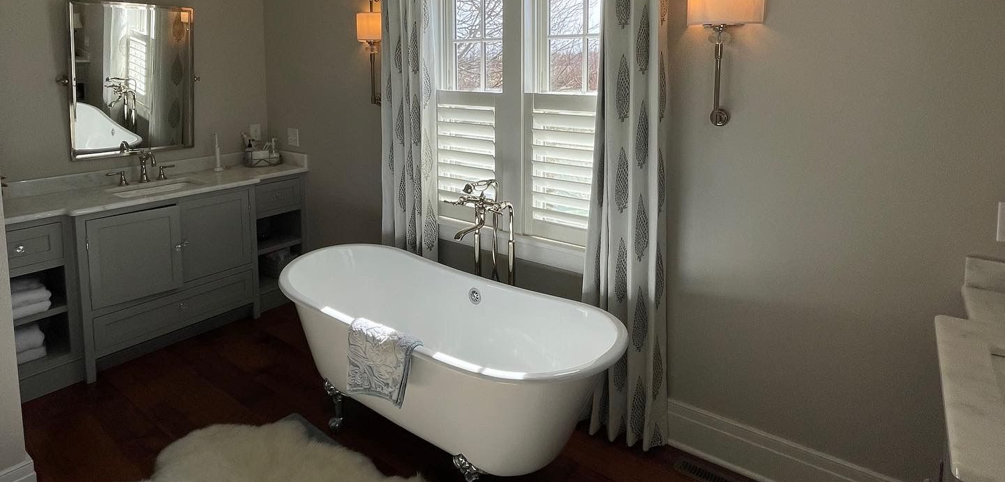Elegant bathroom with a clawfoot tub, interior shuttters, and a window with patterned curtains.