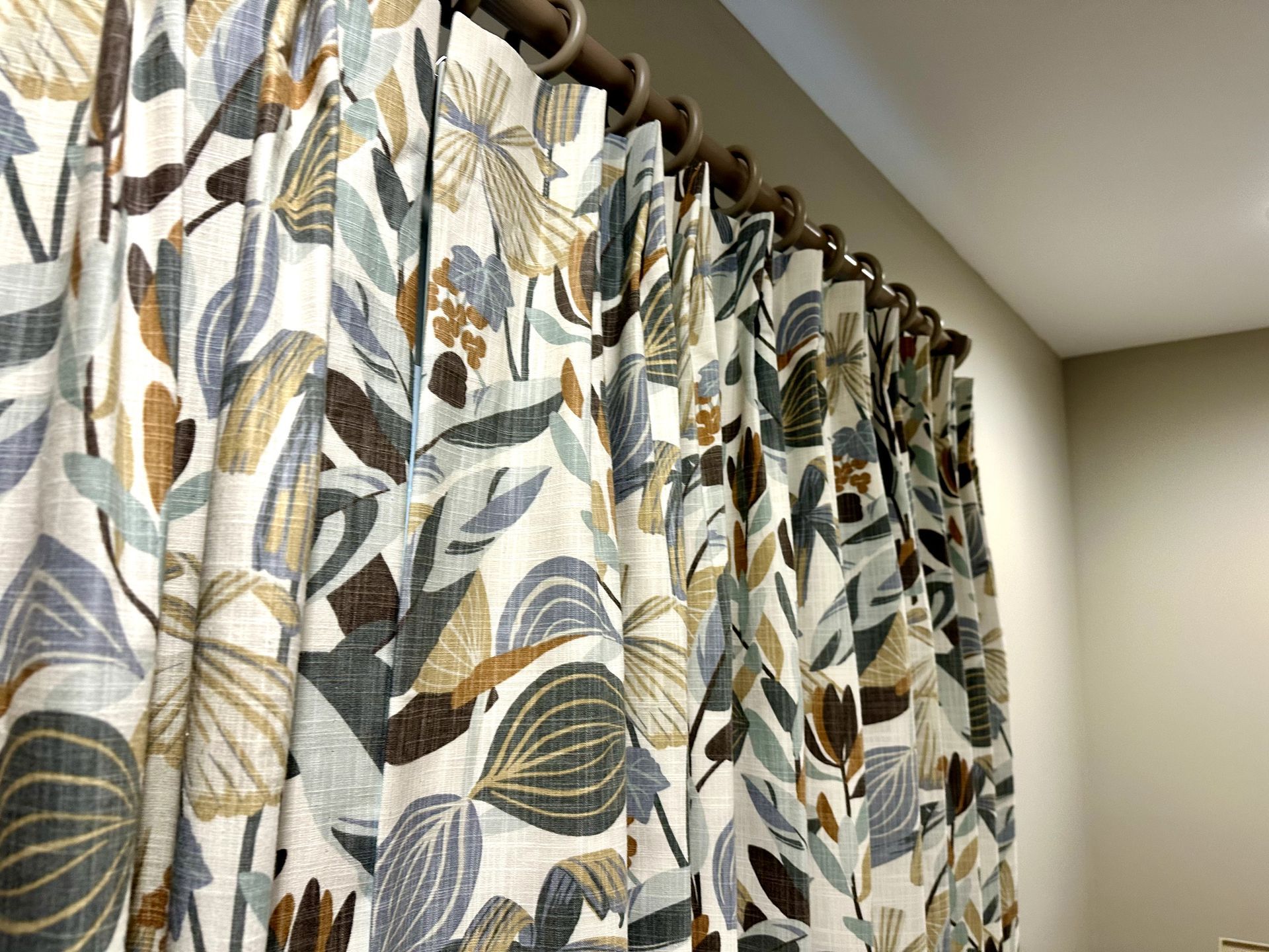 Floral print curtains hanging from a bronze rod. Cream, blue, and brown plant pattern.