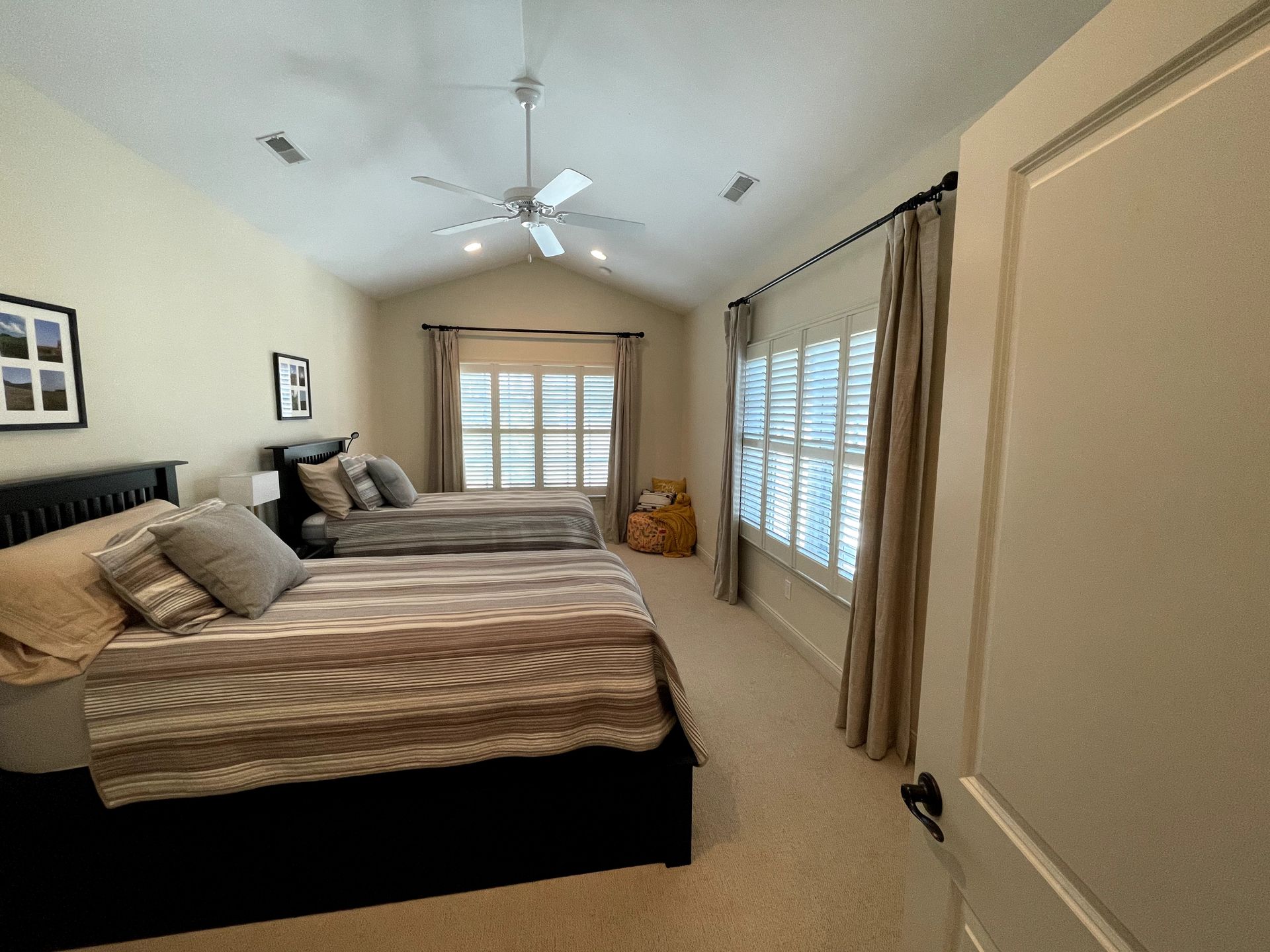 Bedroom with two beds, beige walls, tan curtains, and natural light from windows.