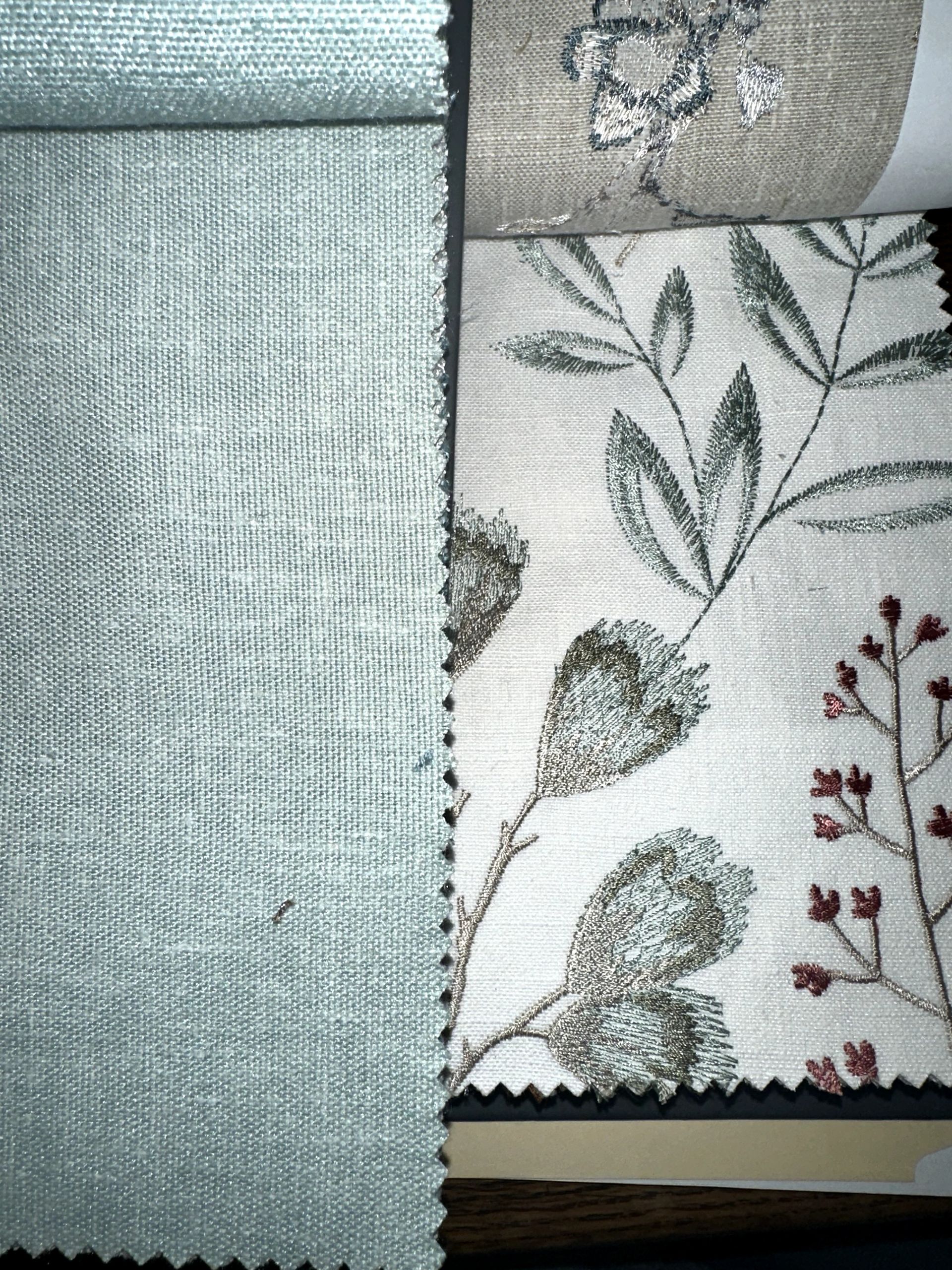 Fabric swatches, one a solid light blue, others with floral embroidery in shades of green, brown, and red.
