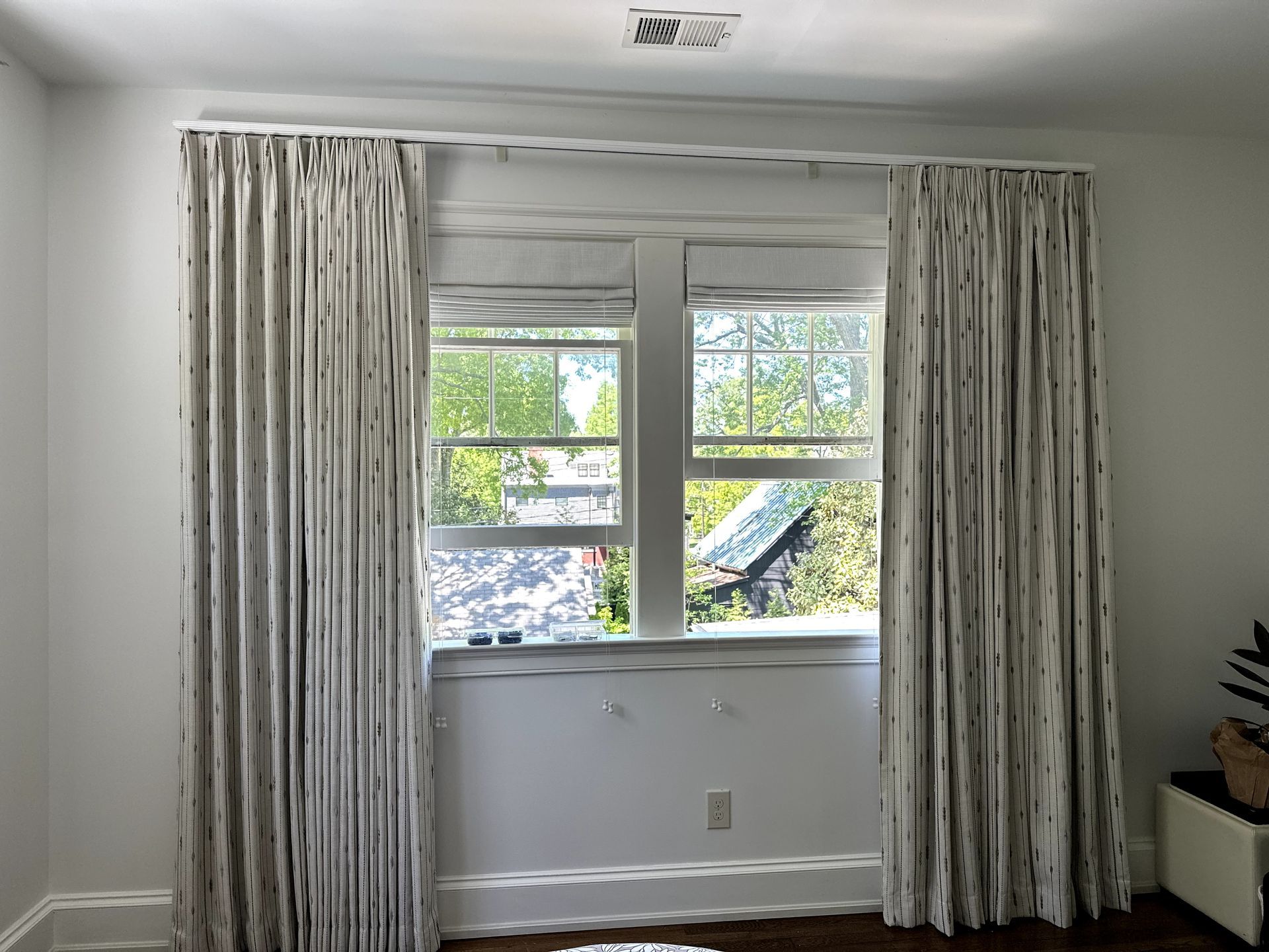 Window with white frame, sheer shades, and patterned, floor-length curtains. Green trees visible outside.
