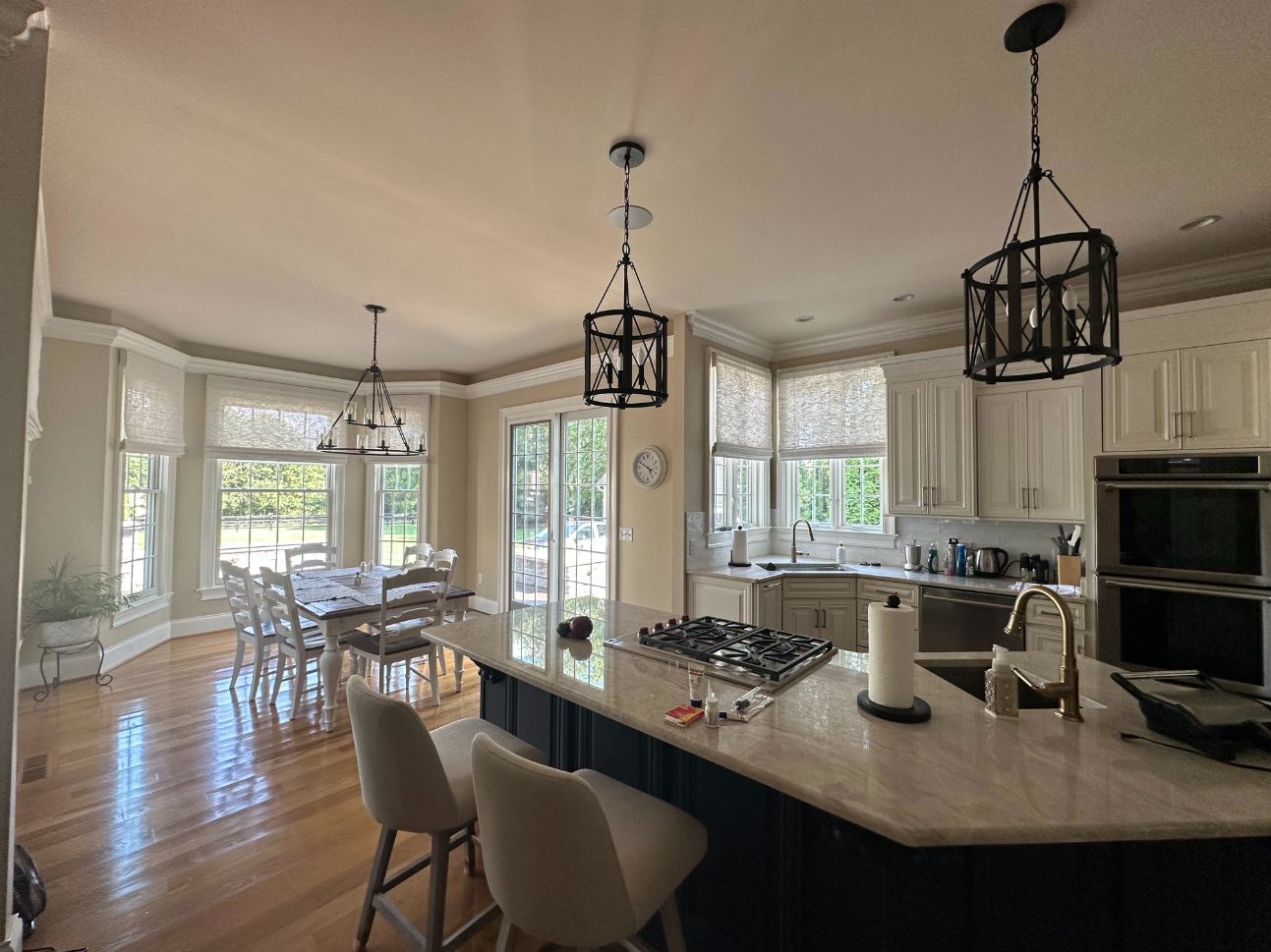 Modern kitchen with a dark island, marble countertops, light wood floors, and dining area with large windows.