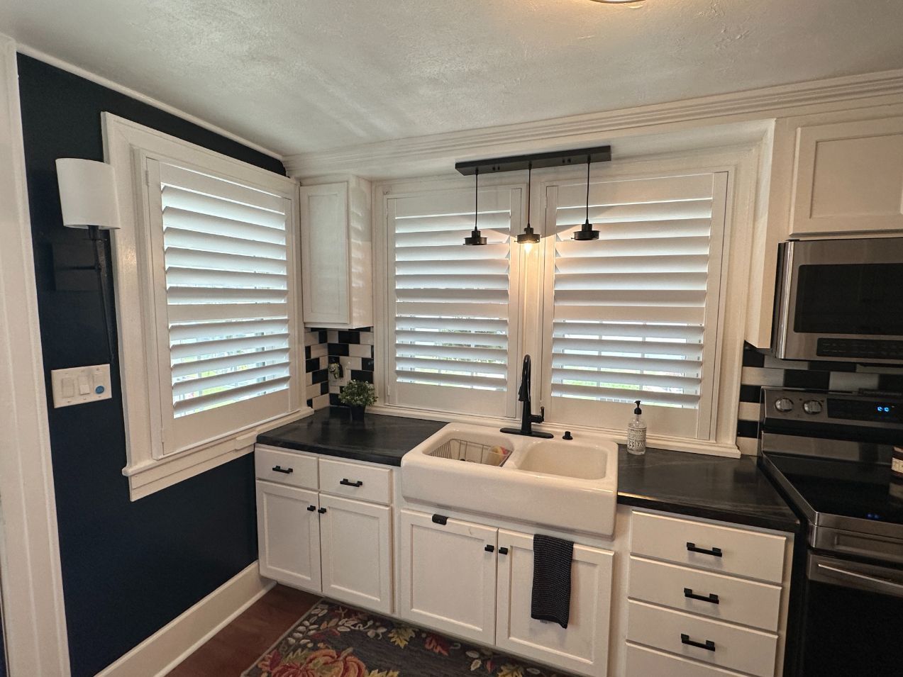 Kitchen with white cabinets, farmhouse sink, black countertops, and white shutters.