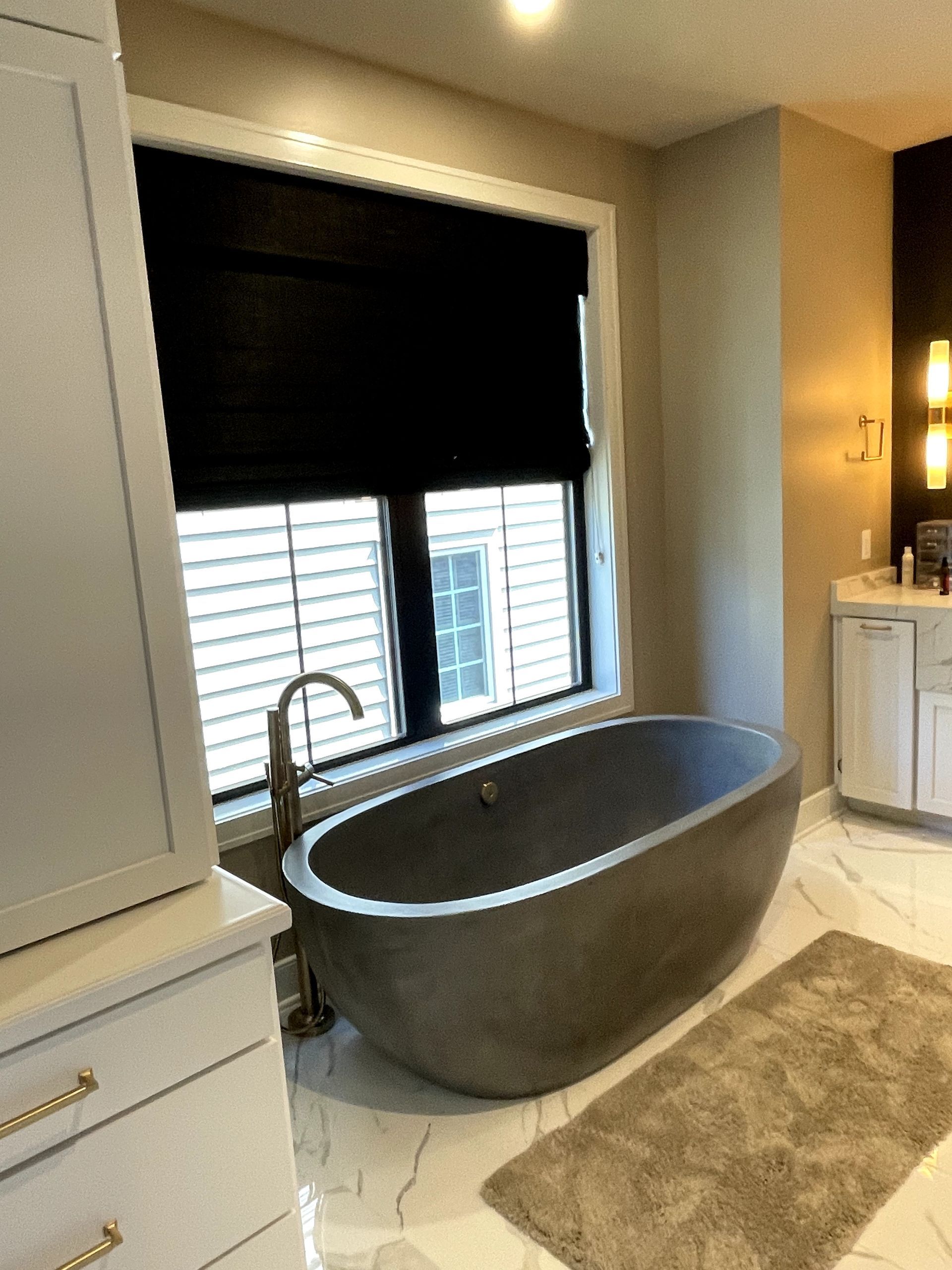 Modern bathroom with a gray soaking tub near a window with black shades.