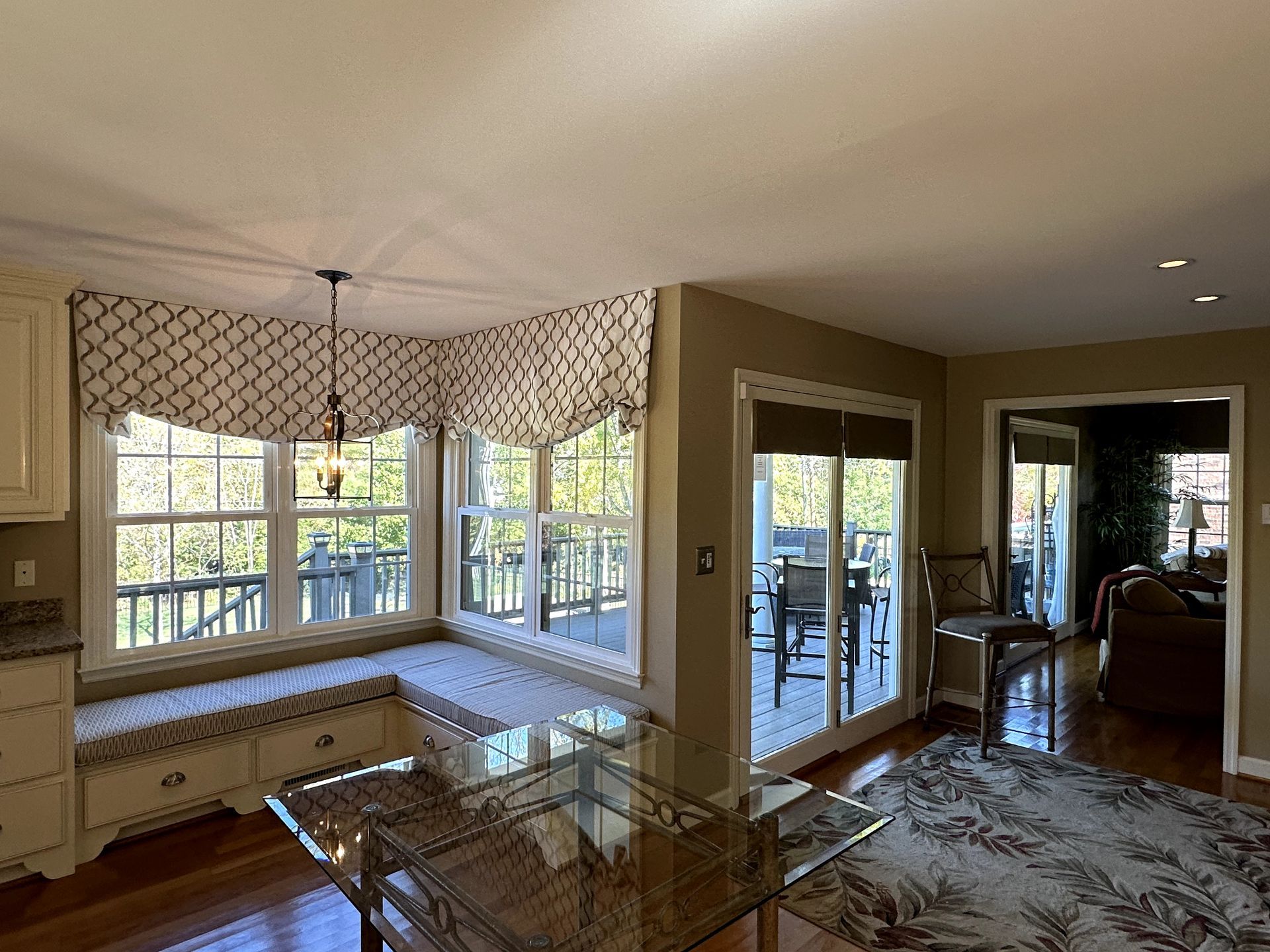Kitchen with window seat, glass table, and patterned valance; sliding glass door to a deck.