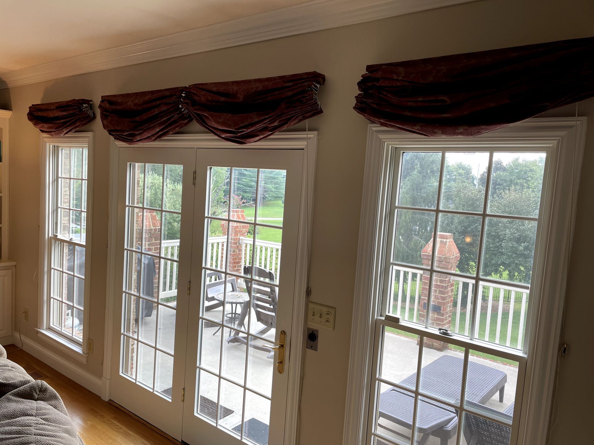 Three windows with burgundy valances overlooking a deck with seating.