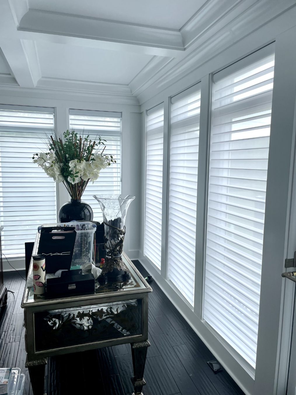 Interior with white window treatments, a mirrored table, and flower arrangement.