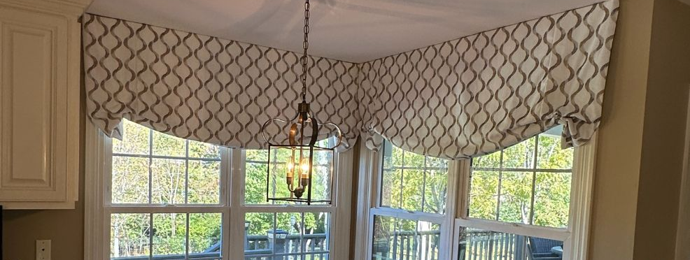 Bright kitchen corner with bay windows, white patterned valance, and a hanging light fixture