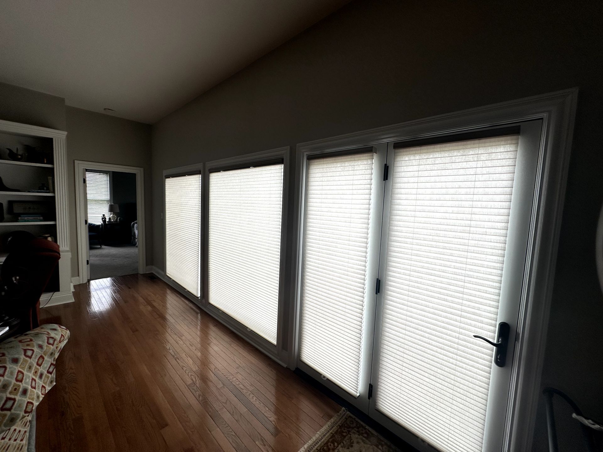 Interior view: sliding glass doors with white blinds, hardwood floor, and a glimpse of another room.