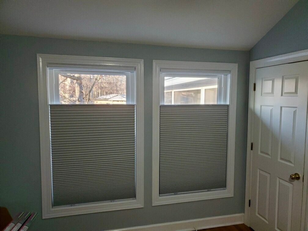 Two windows with gray honeycomb shades, white trim, and a closed white door in a room with blue walls.