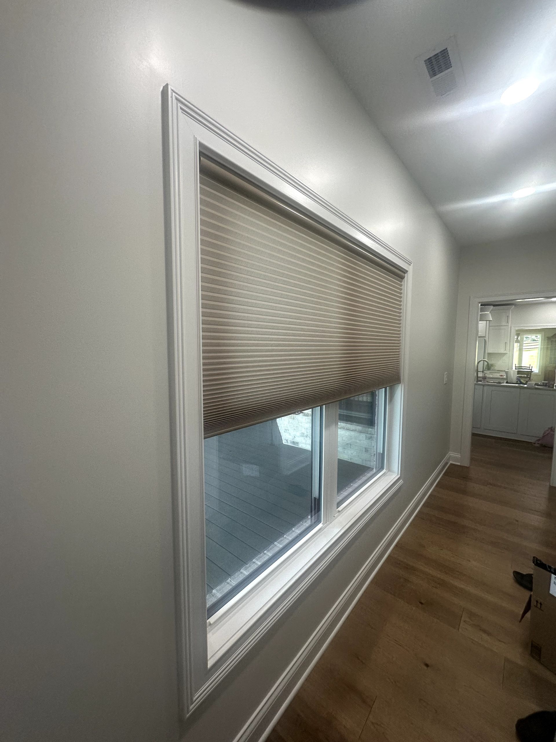 Window with a beige Roman shade, set in a white-framed opening on a light gray wall.