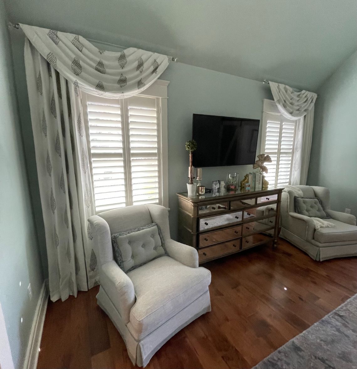 Bedroom with two armchairs, a dresser with TV, shuttered windows, and custom drapery.