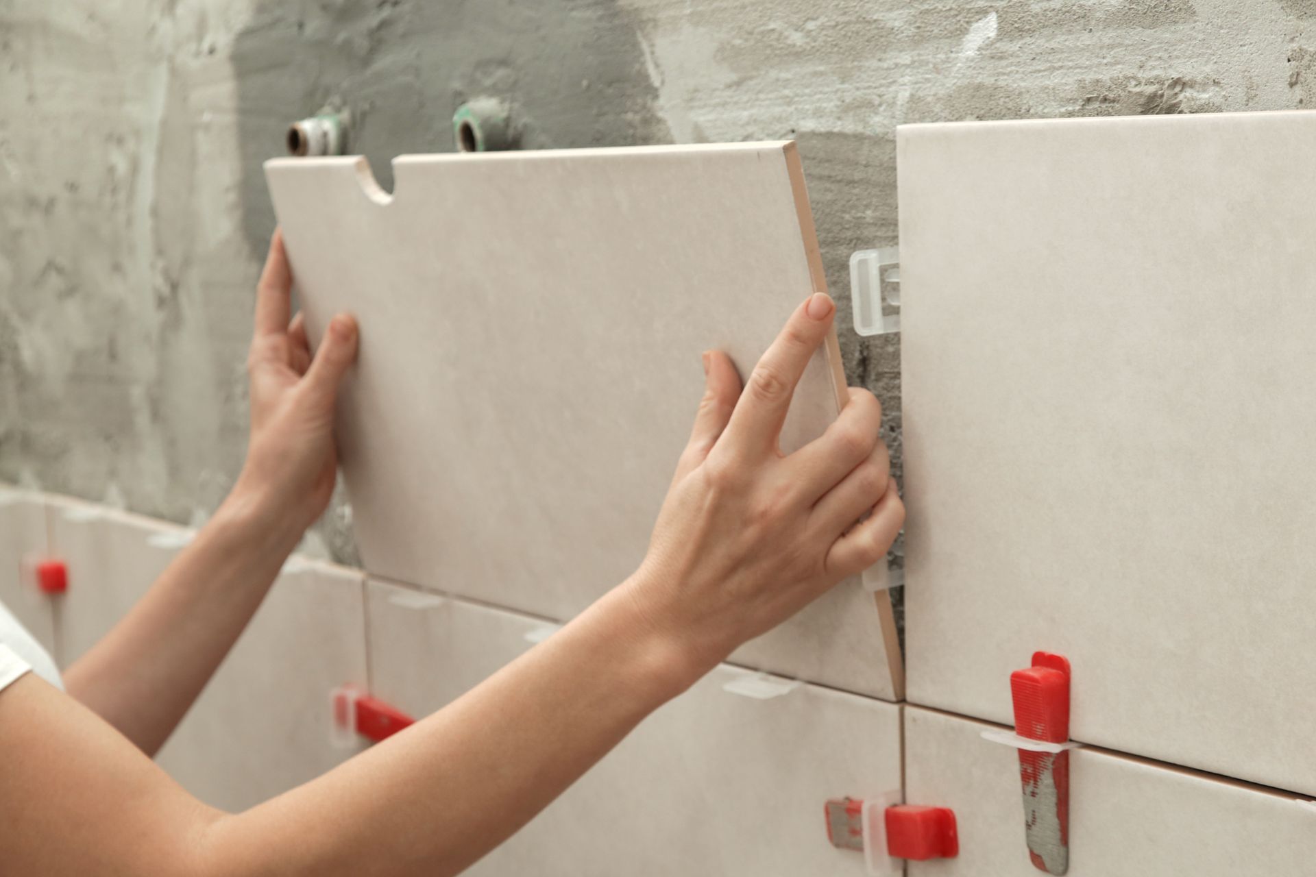 A woman is installing tiles on a wall.