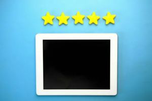 A tablet with a black screen rests on a blue background below a horizontal row of five yellow stars.