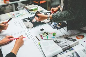 People collaborating at a table with pens, paper, and magazine cutouts for a design or brainstorming project.
