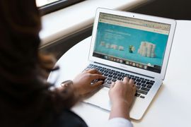 A person typing on a MacBook Air, with a bright blue webpage featuring small white shapes visible on the screen.