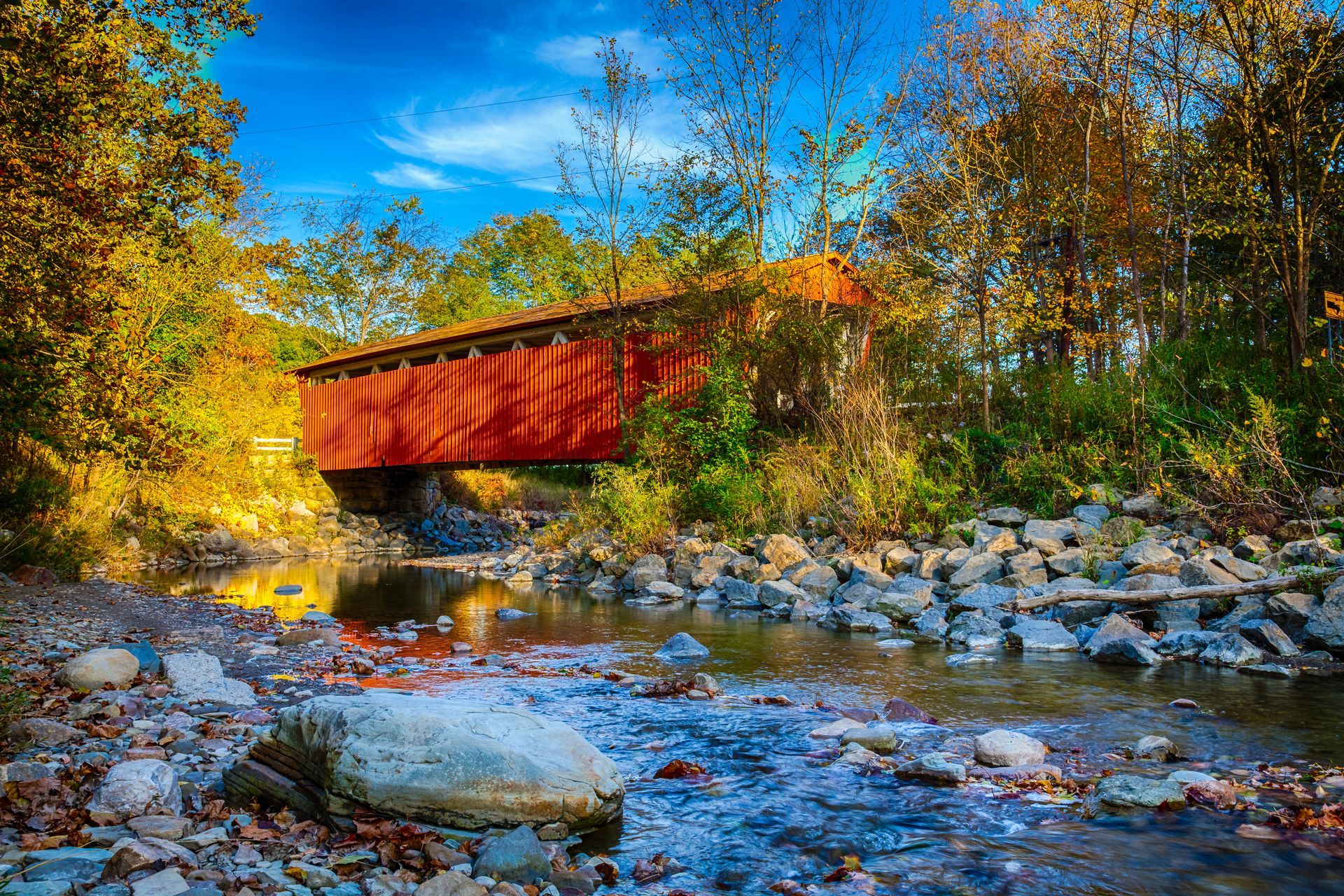 Red covered bridge over a rocky creek in autumn.