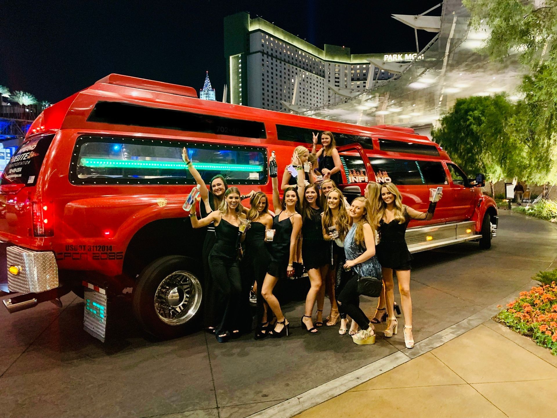 A group of women are standing in front of a red limousine.