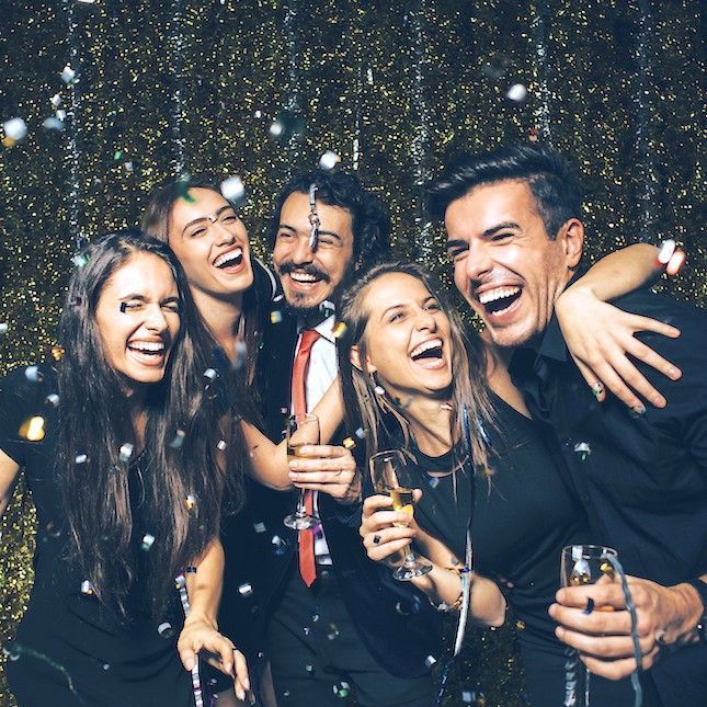 A group of people are laughing and holding champagne glasses at a party.