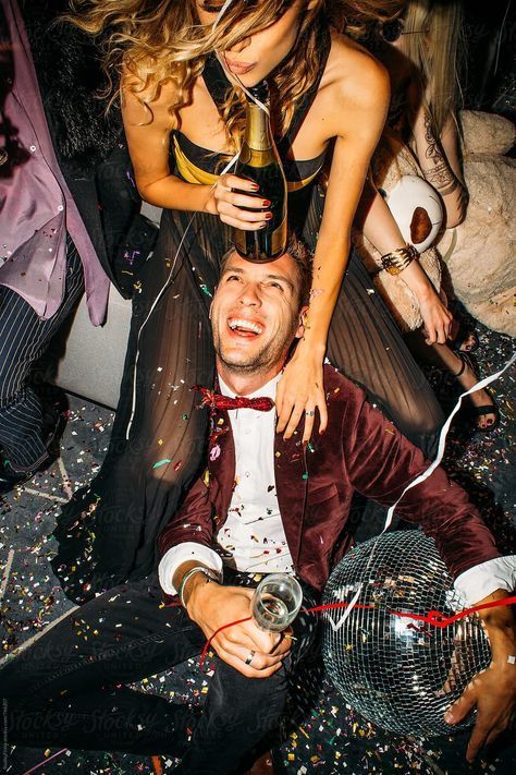 A woman is sitting on a man 's back at a party holding a bottle of champagne.
