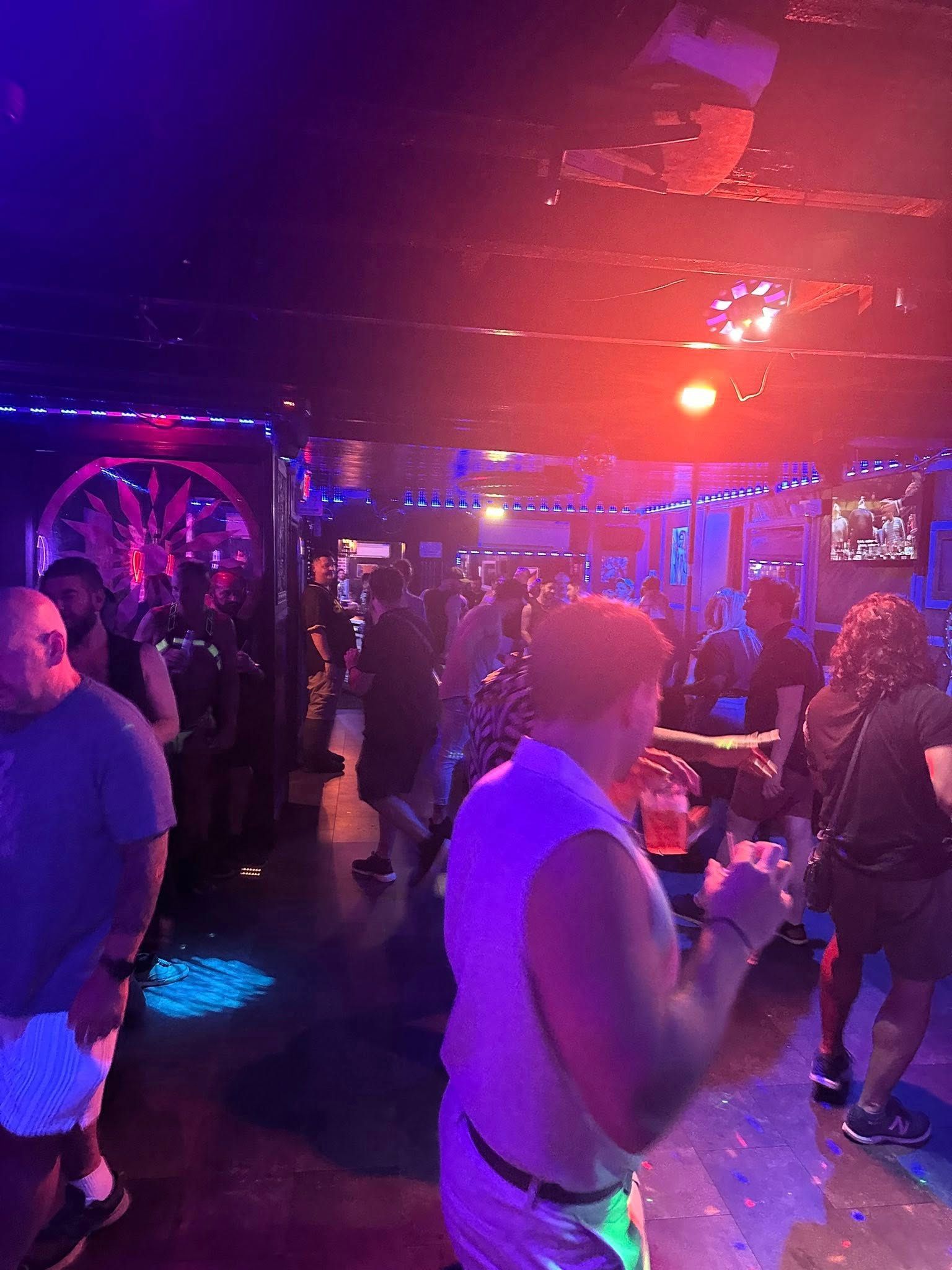 People dancing in a dimly lit club with blue and red lights; some are drinking.