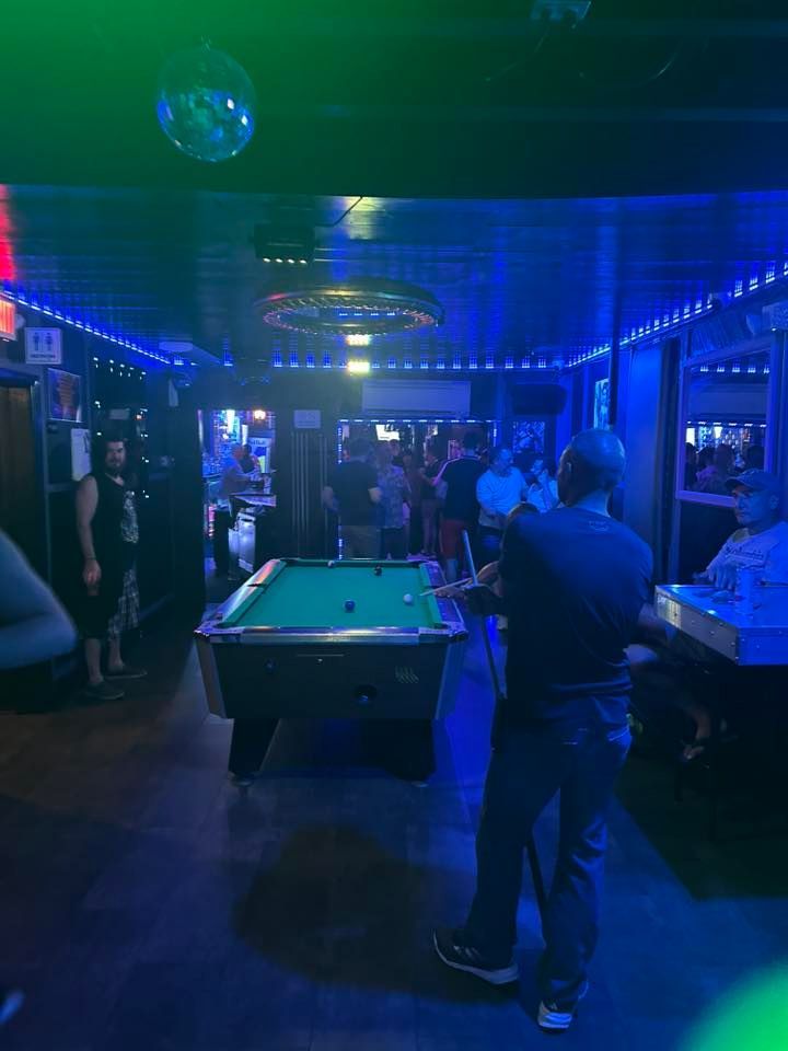 A dimly lit bar with people playing pool, blue and green neon lights.