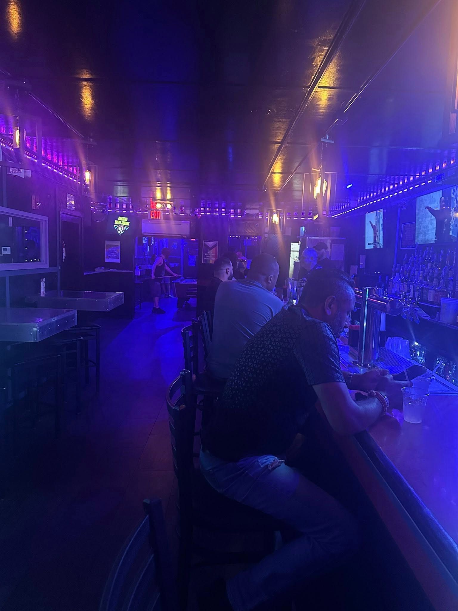 Bar interior with people. Low lighting, mostly purple. People seated at the bar and tables.