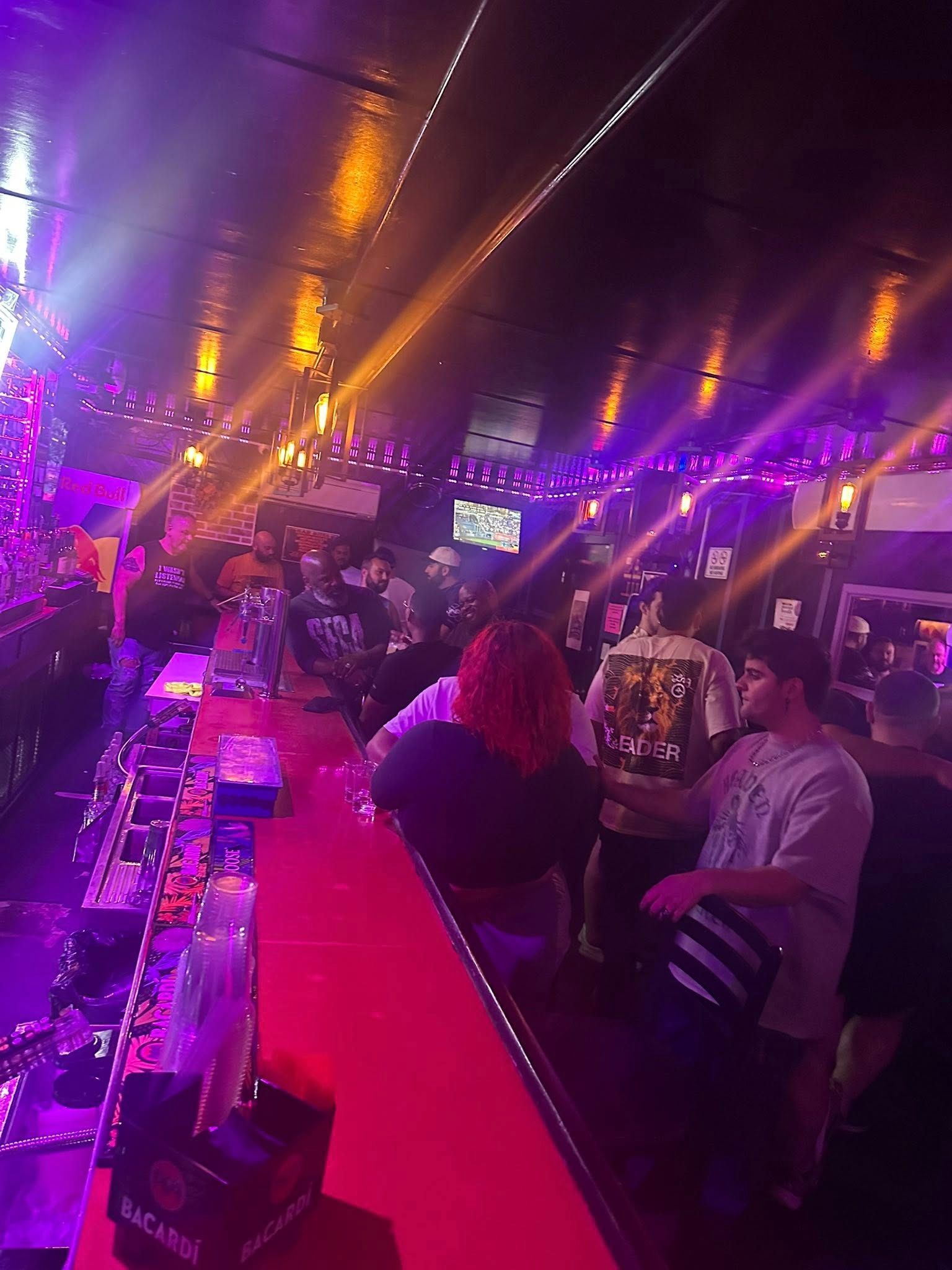 Bar scene with patrons, red bar, and purple and yellow lighting.