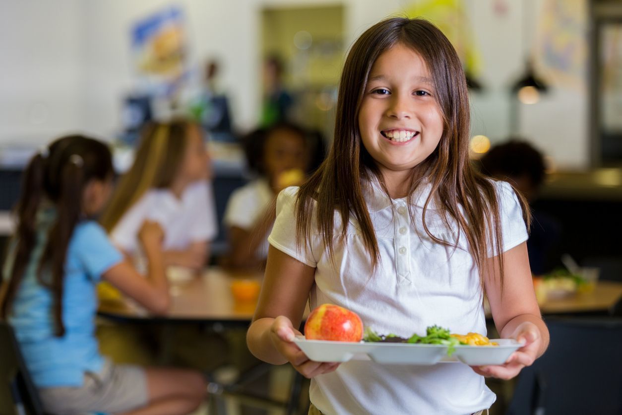 Child holding a cafeteria tray and smiling toward the viewer