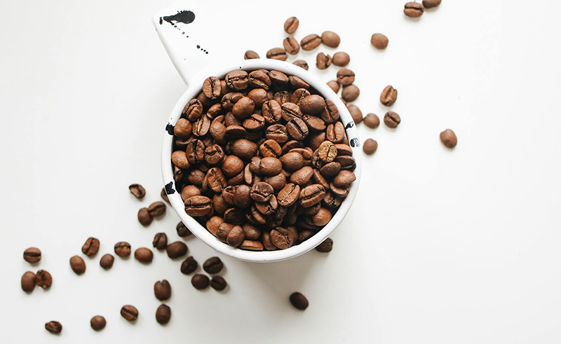 Coffee beans in a cup and spilled onto a white table