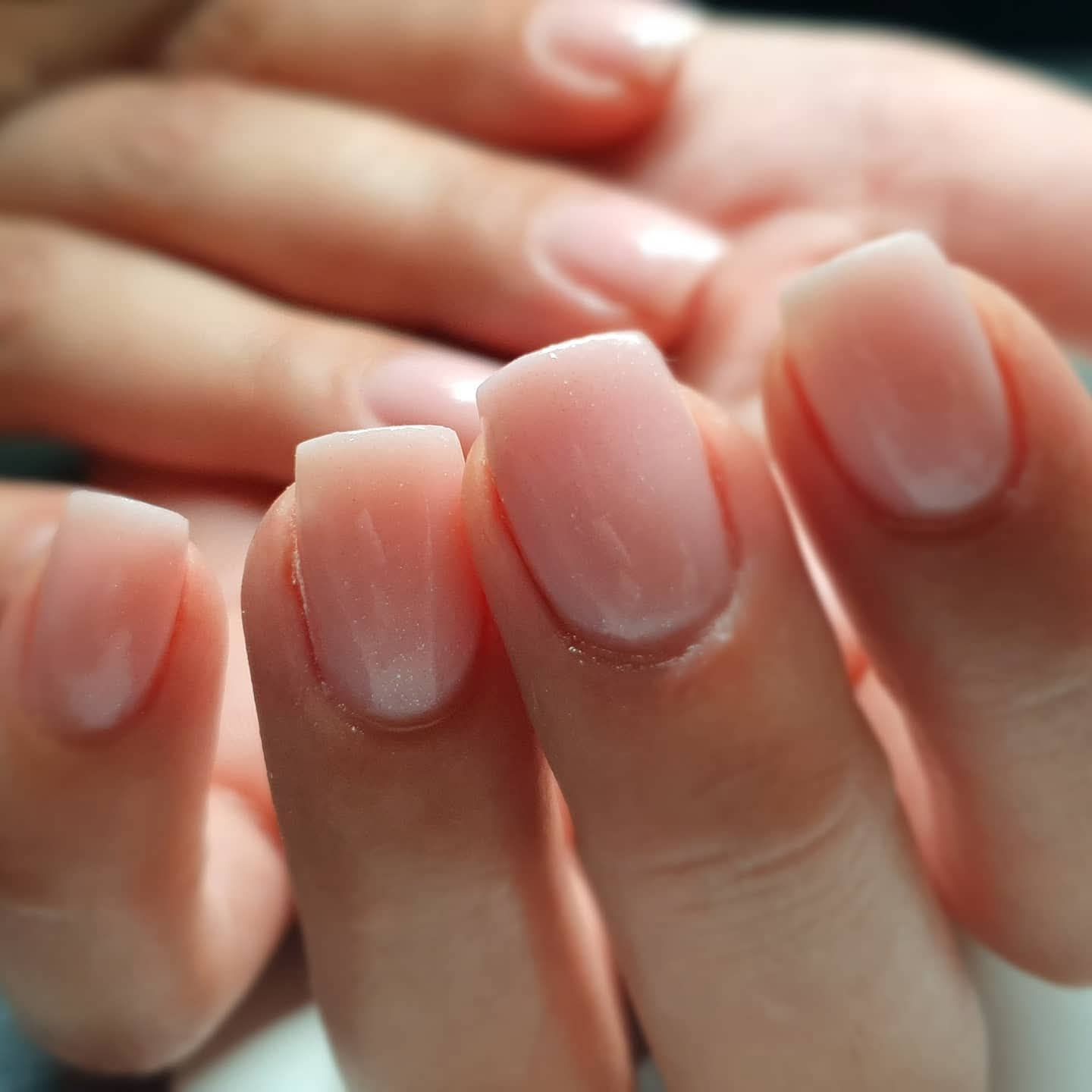 Close-up van een hand met vierkante, huidkleurige gelnagels.