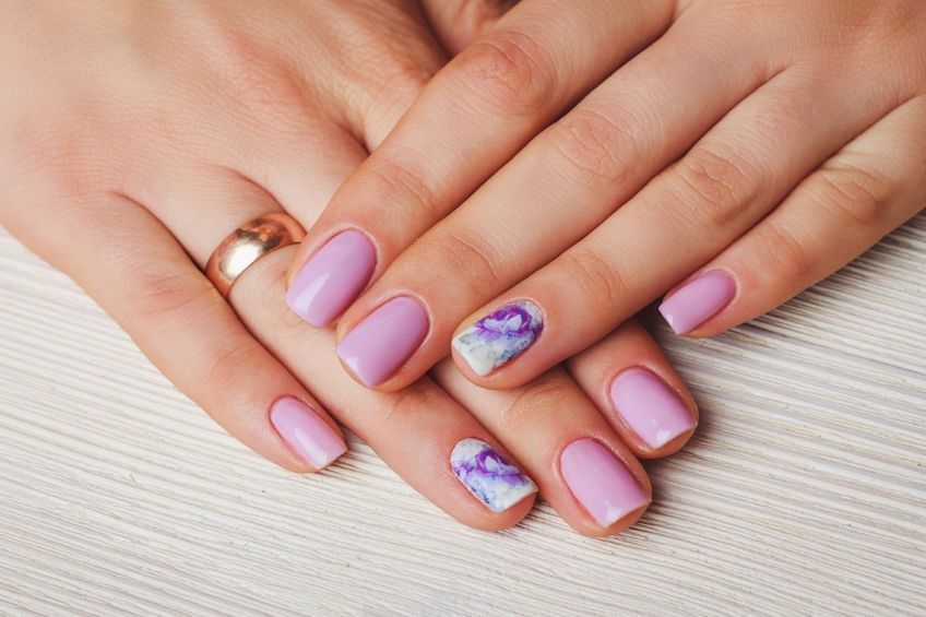 Handen met verzorgde nagels, in diverse pastelkleuren en met verschillende designs, naast flesjes nagellak.