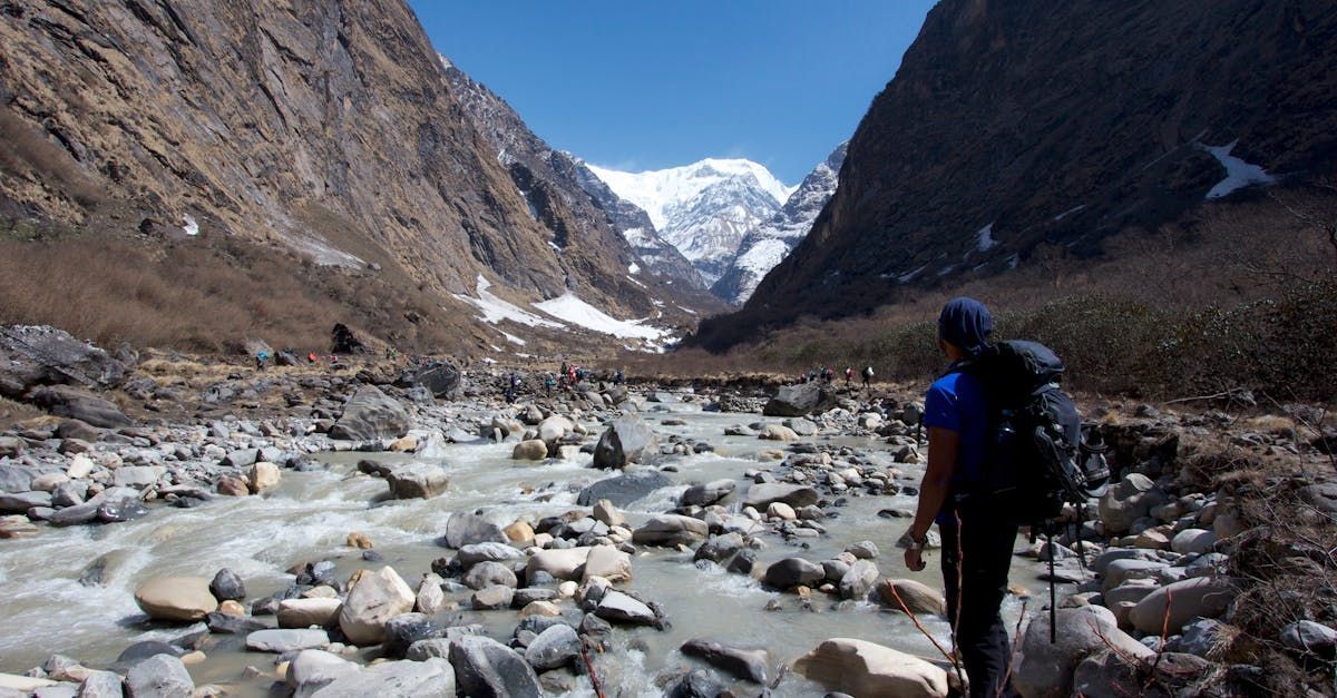 A person with a backpack is walking along a river in the mountains.