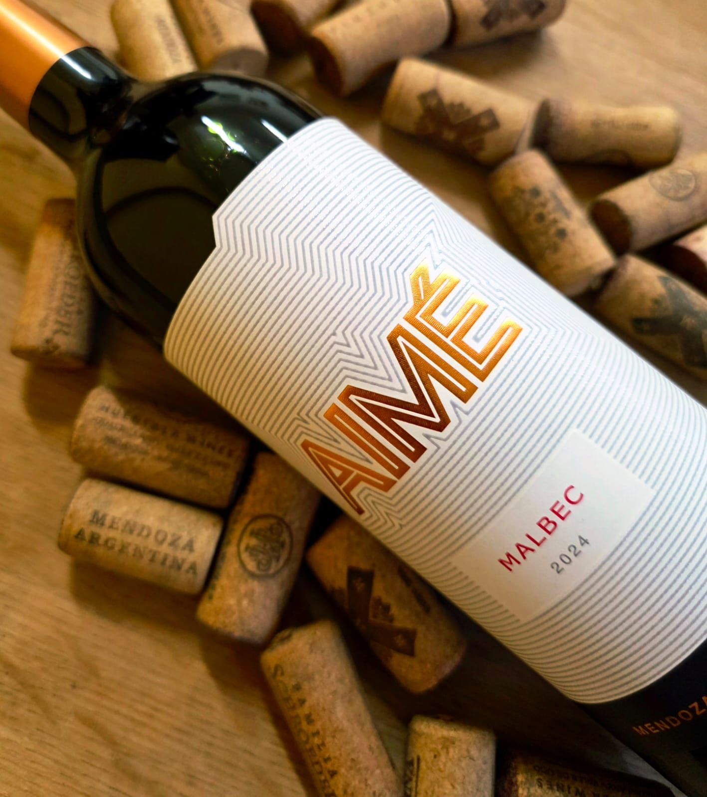 Una botella de vino Aime Malbec 2024 descansa sobre una colección de corchos